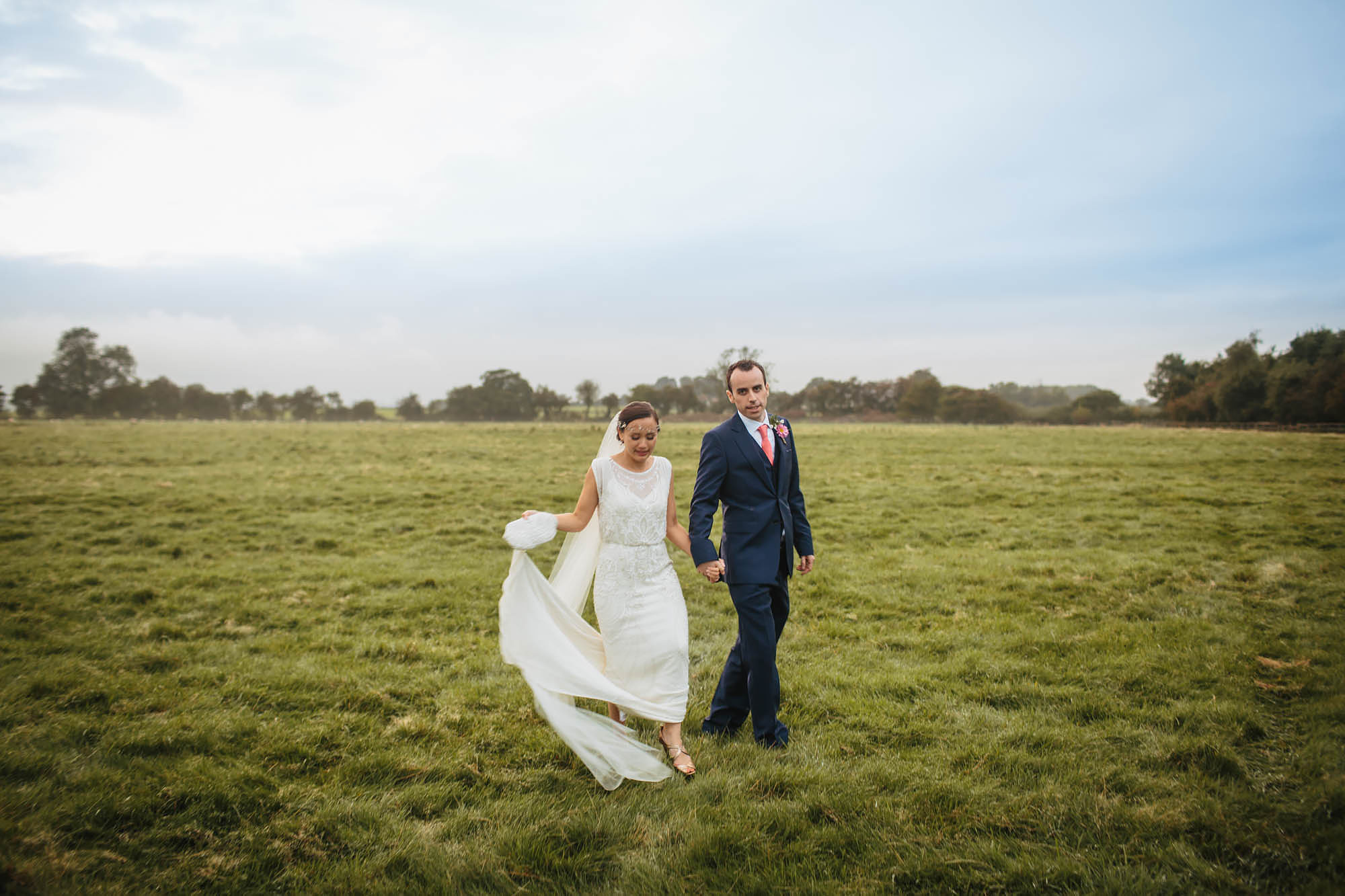 Bride and groom walking through a field at Hornington Manor