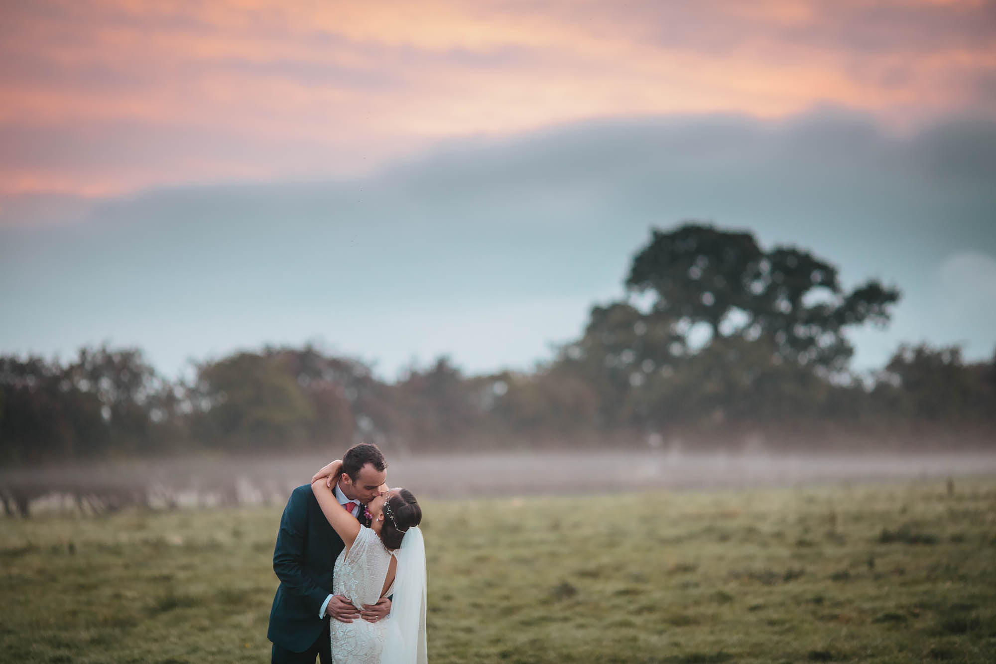 Bride and groom kissing in front of a sunset at a Hornington Manor wedding