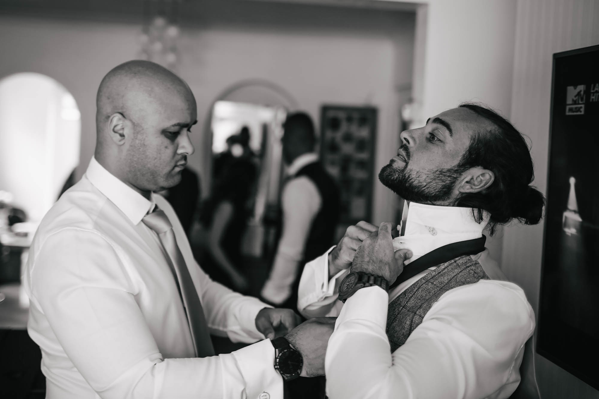Best man helps groom with his tie during wedding prep