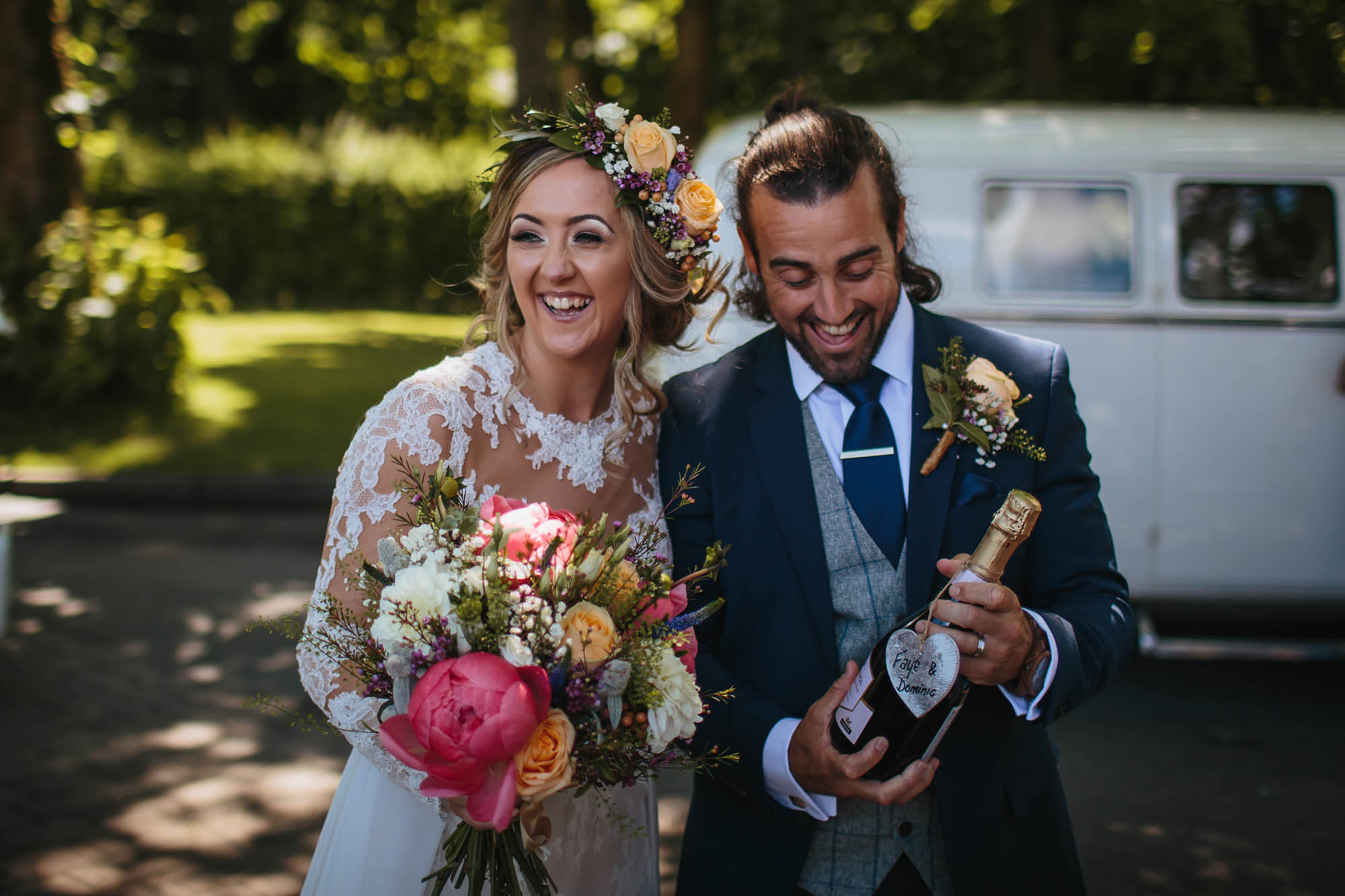 Bride and groom laughing as they hold a bottle of champagne at their wedding