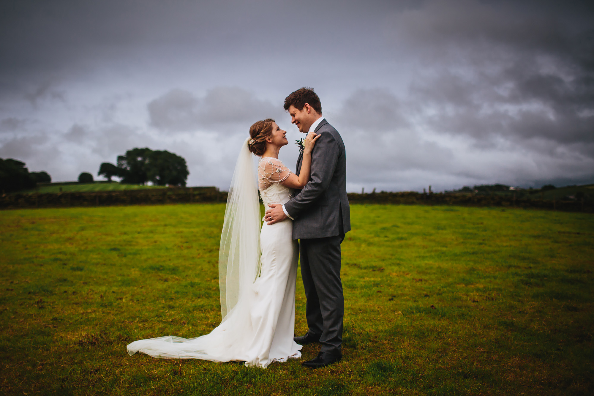 Bride and groom smiling at each other in a field