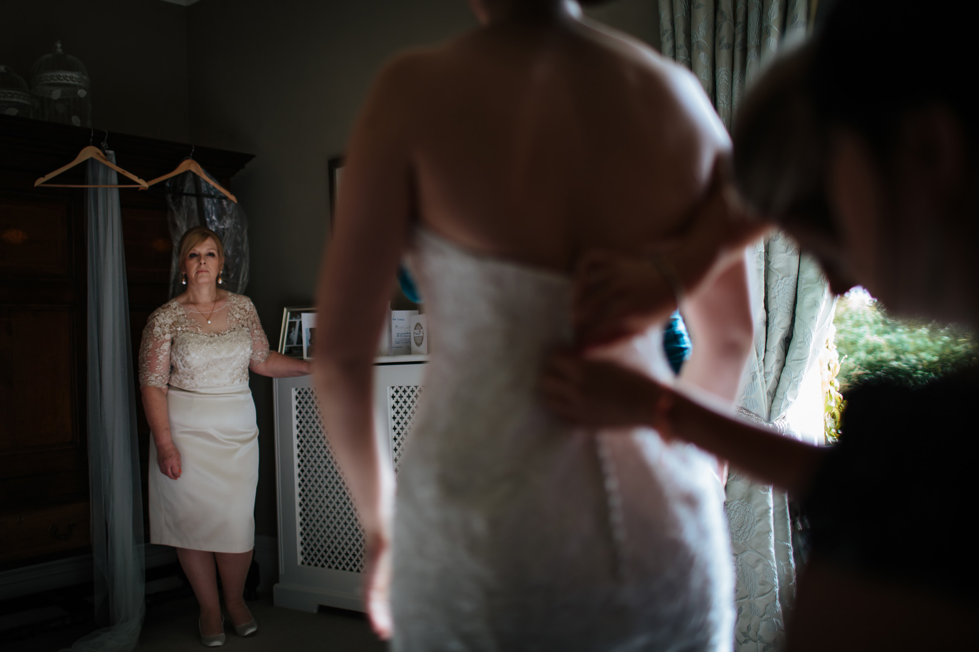 Brides mother watches her daughter have her dress buttoned up