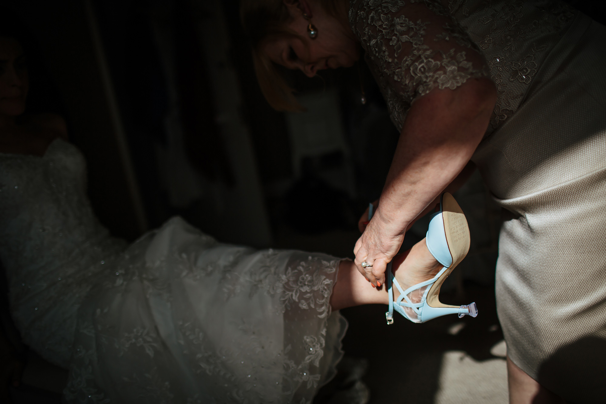 Mother helping bride put her wedding shoes on