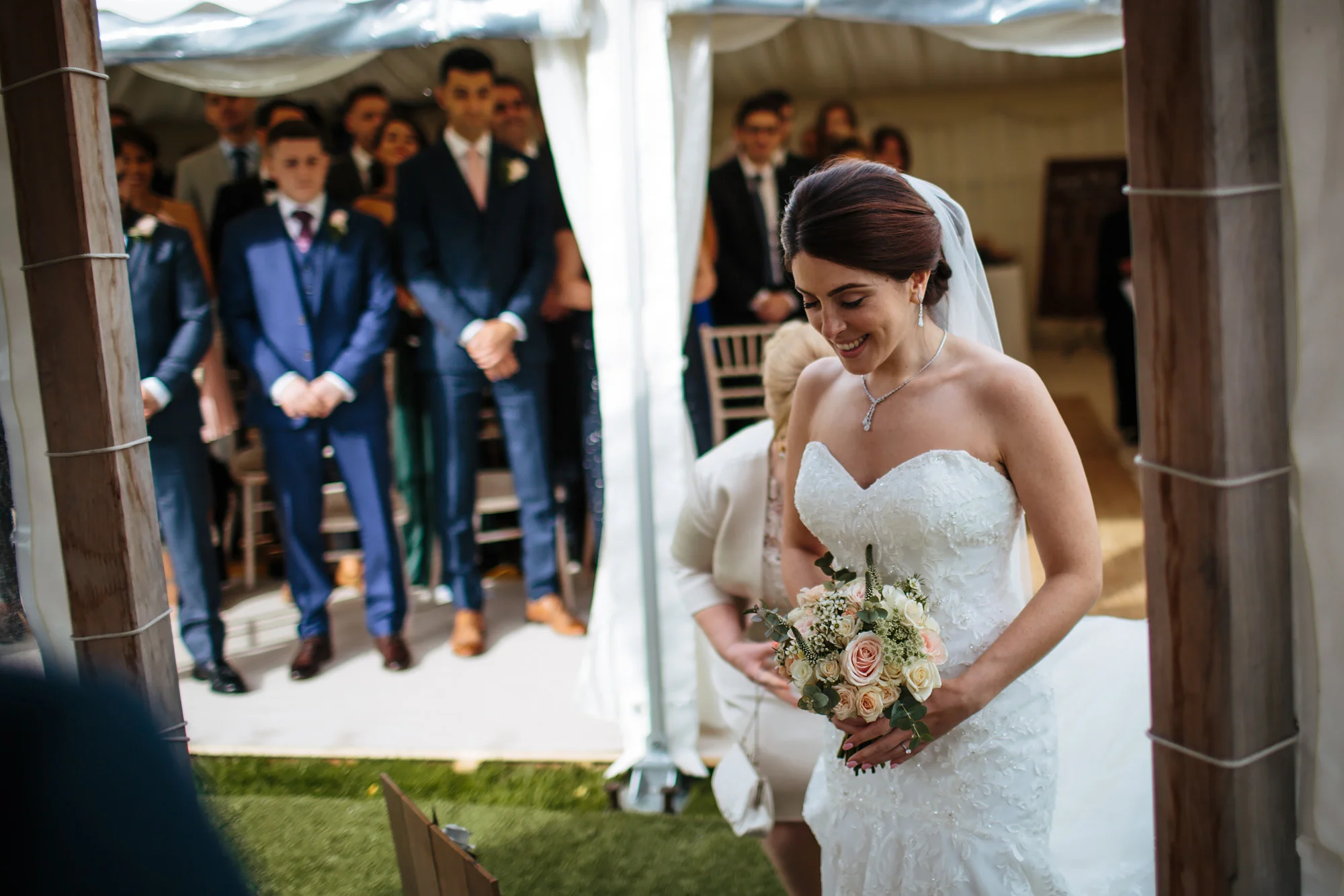 Bride walks down the aisle and enters the ceremony. Groomsmen look on