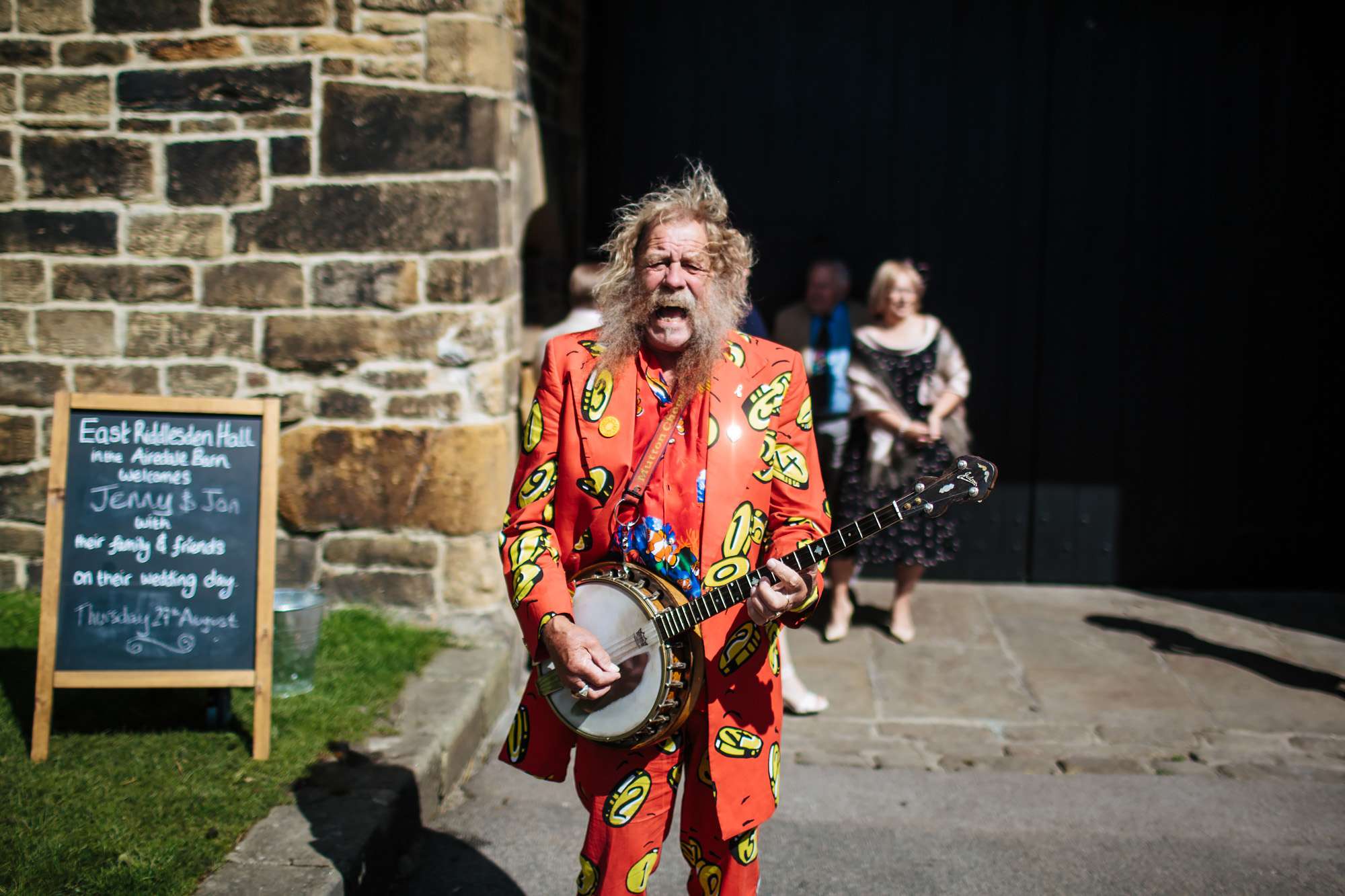 Bearded man playing the banjo in a bright red suit at a wedding