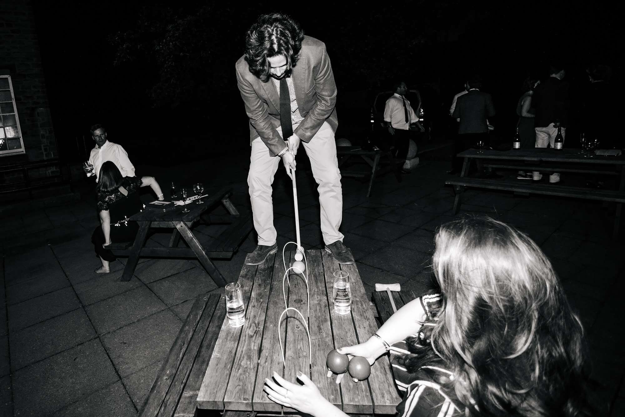 Drunk man at a wedding plays croquet on a picnic table