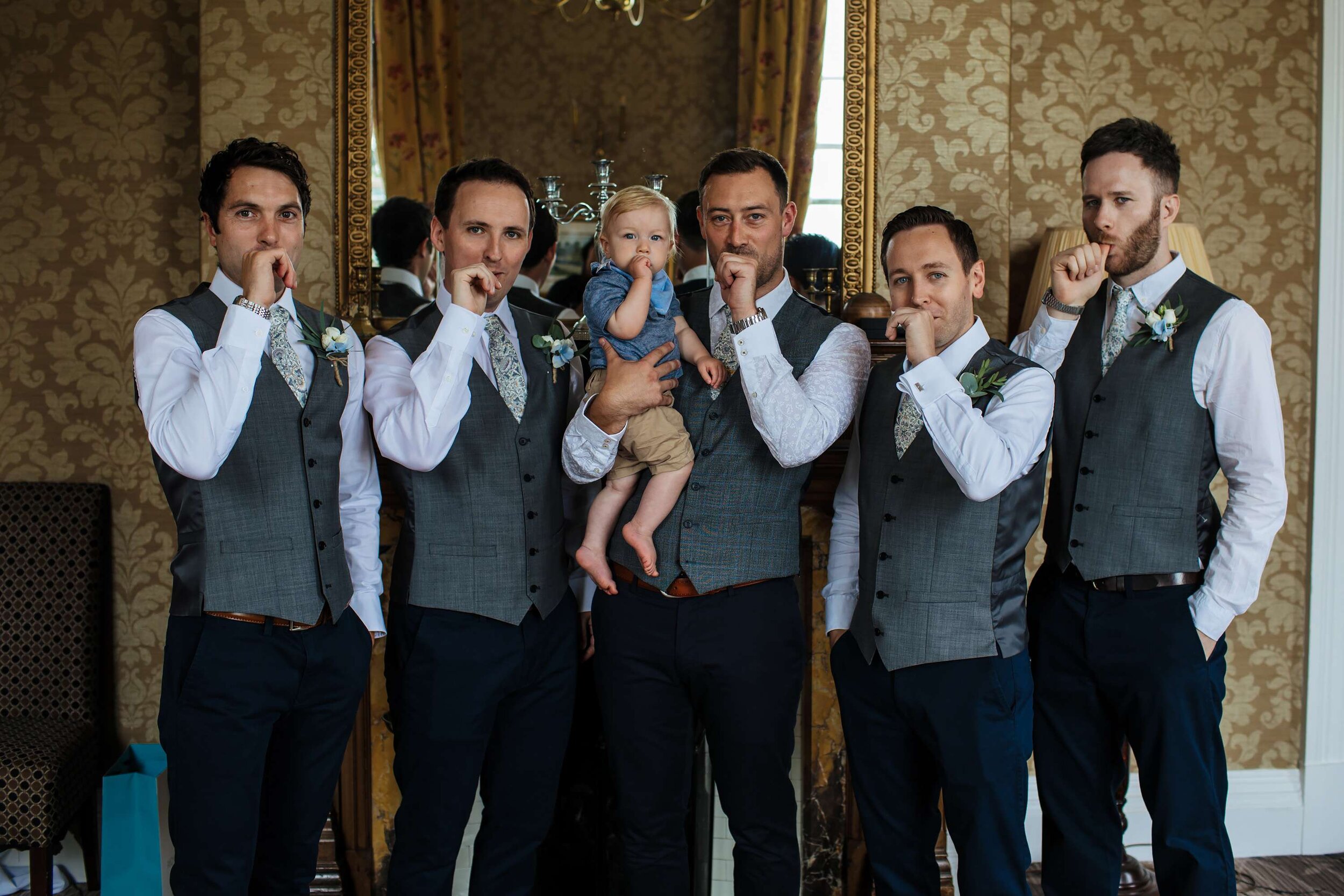 Groomsmen sucking their thumbs with young boy for a photo