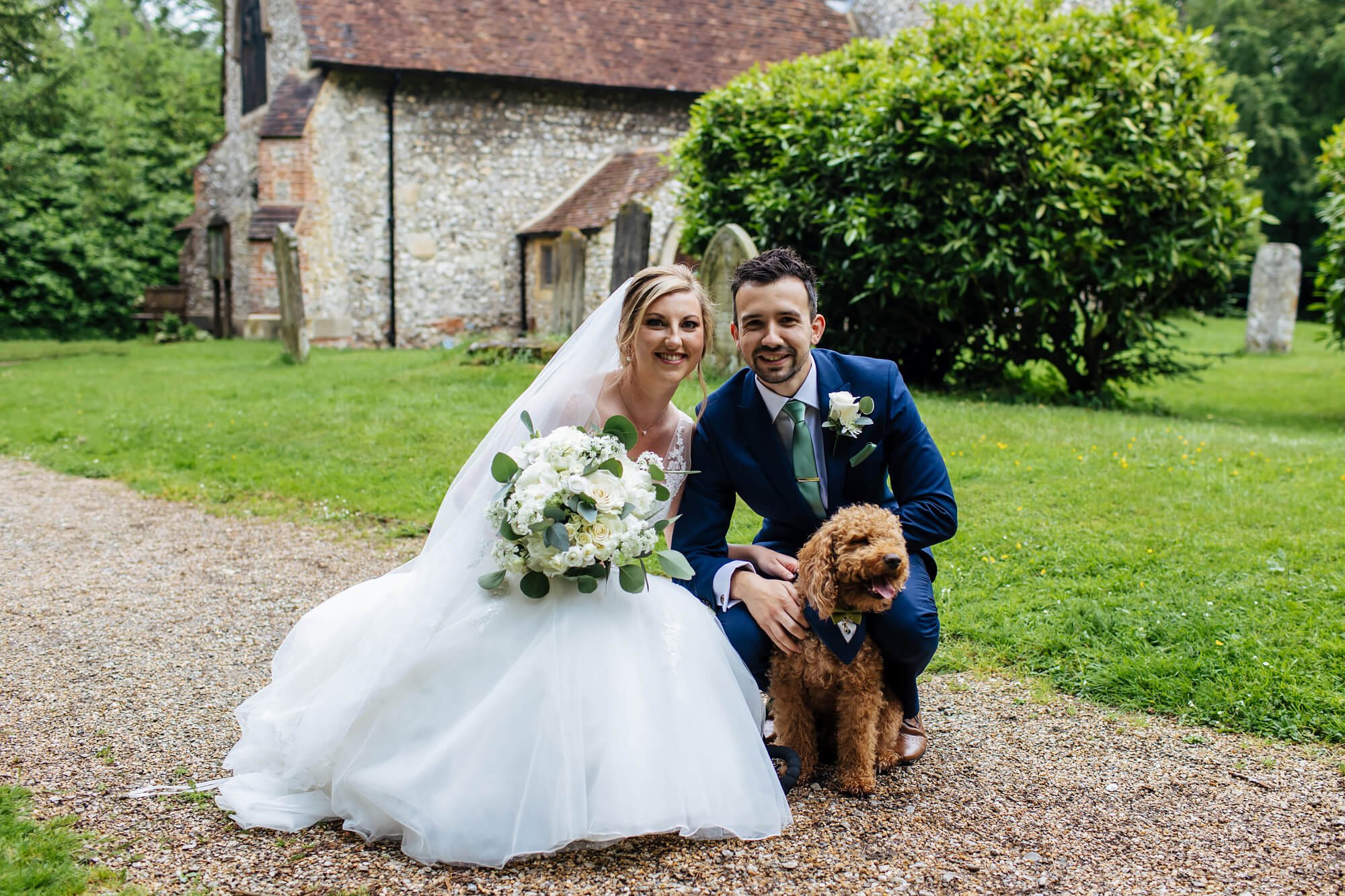 Bride and groom pose with their dog in the church yard