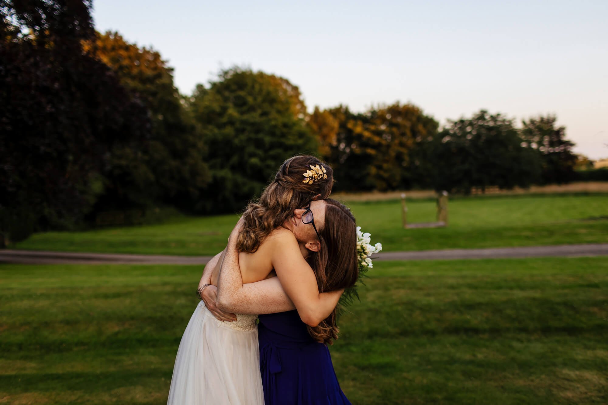 Bride and friend hug in the evening sunshine at a wedding