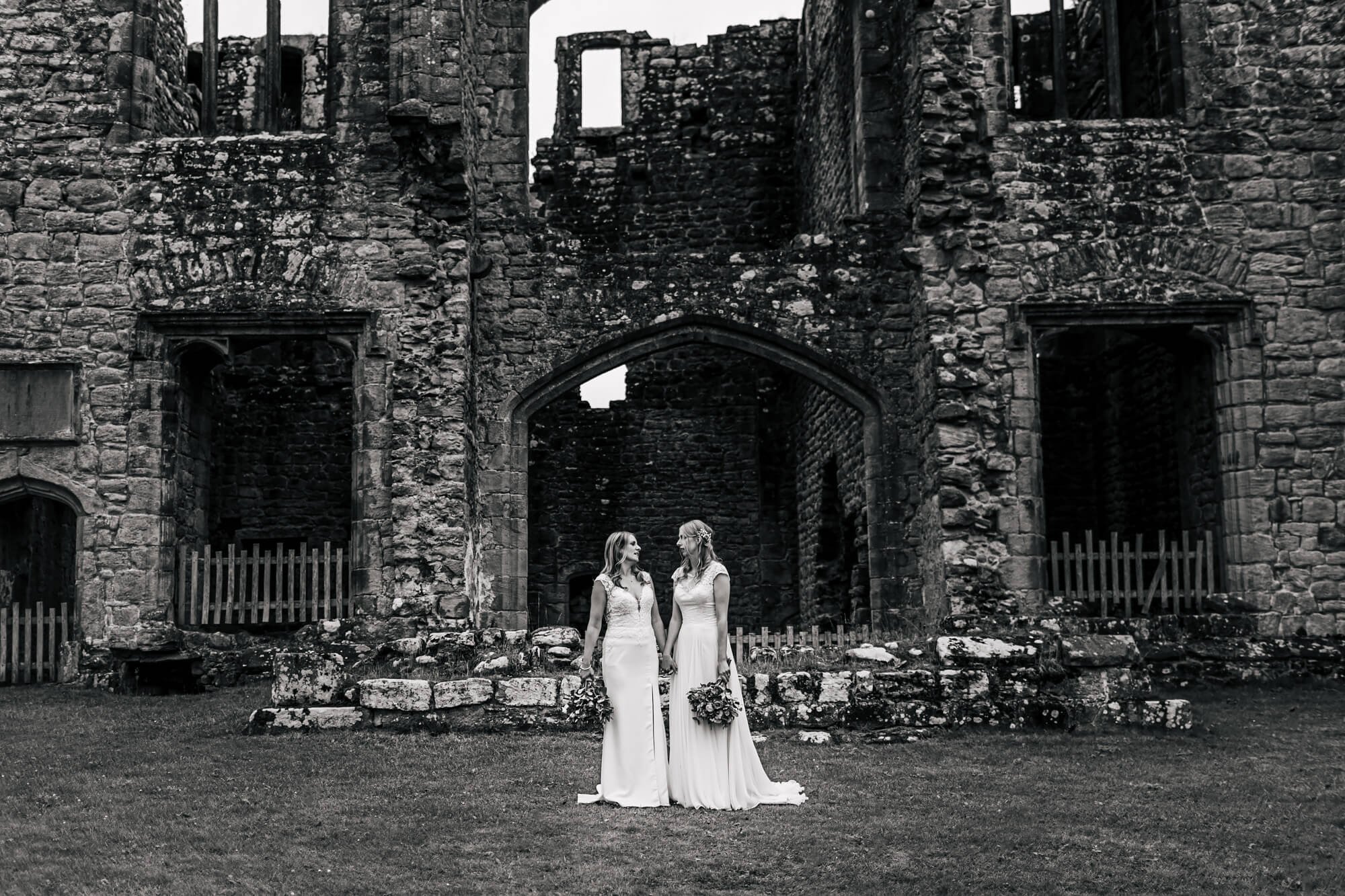 Black and white photo of two brides in front of Barden Tower