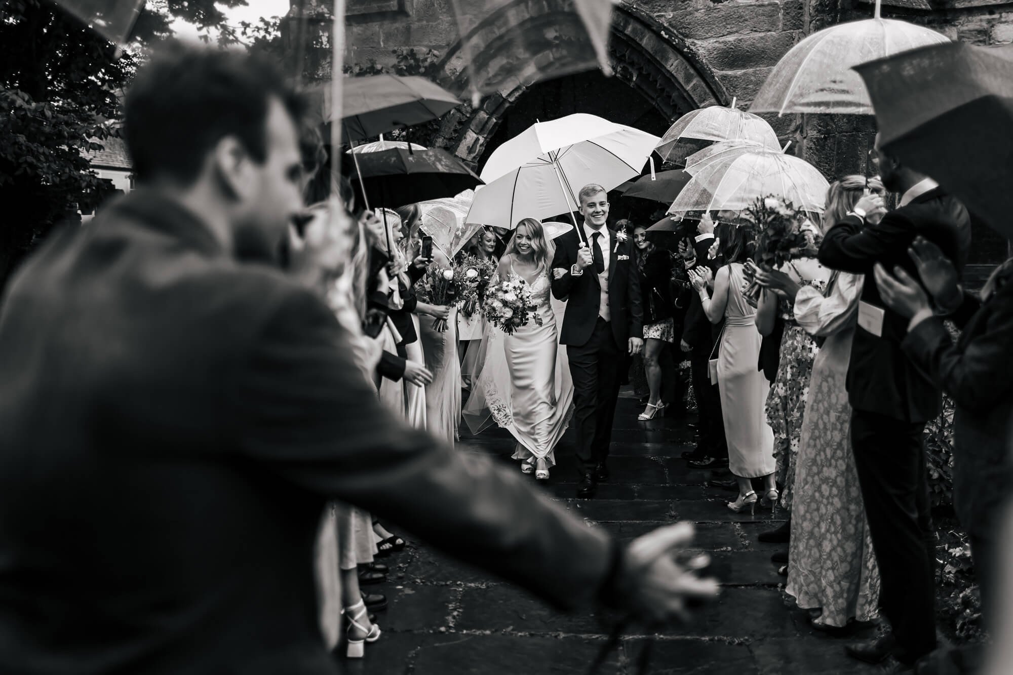 Bride and groom holding umbrellas as the exit their church ceremony