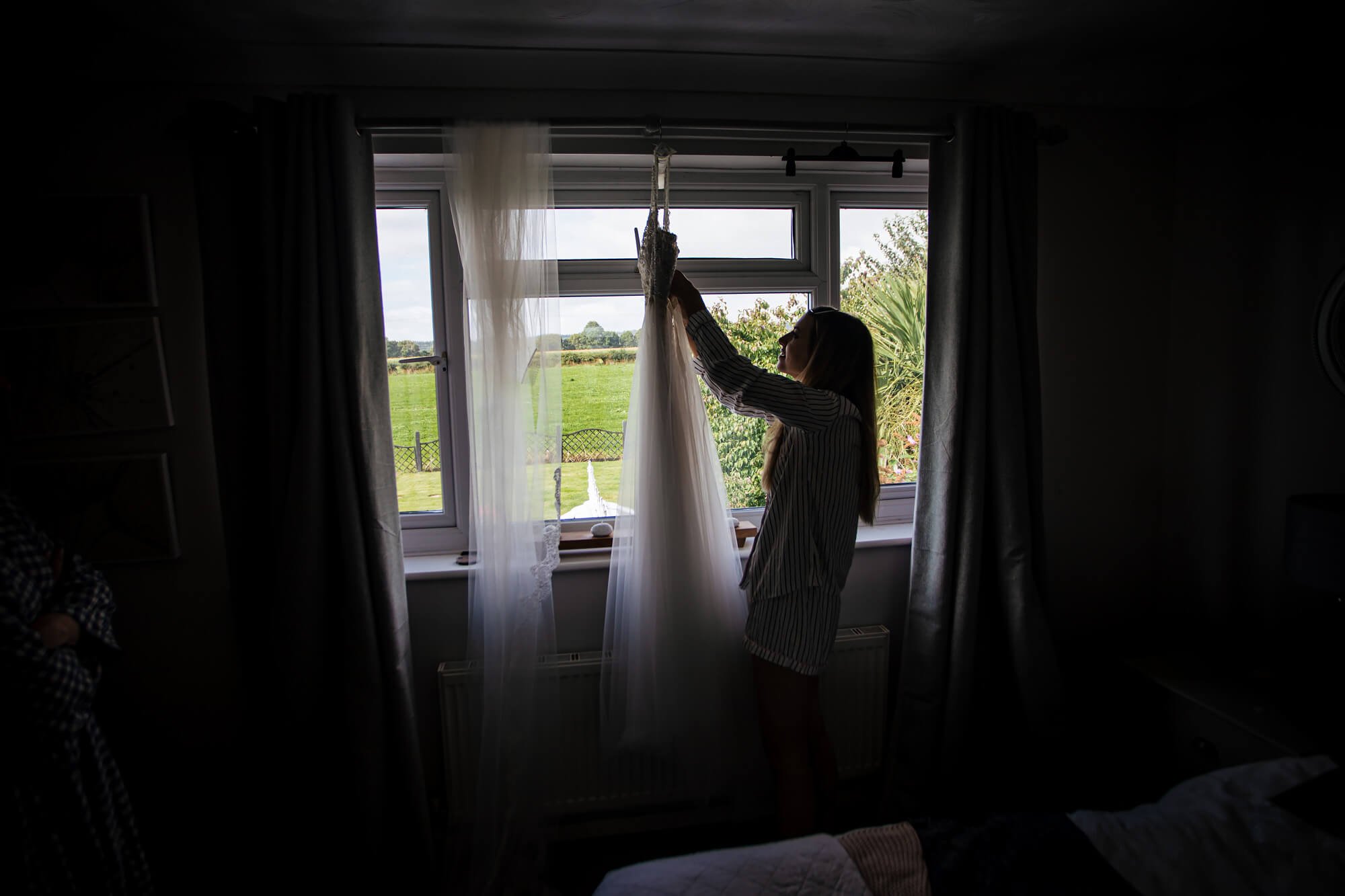 Bride hanging up her wedding dress in the window light