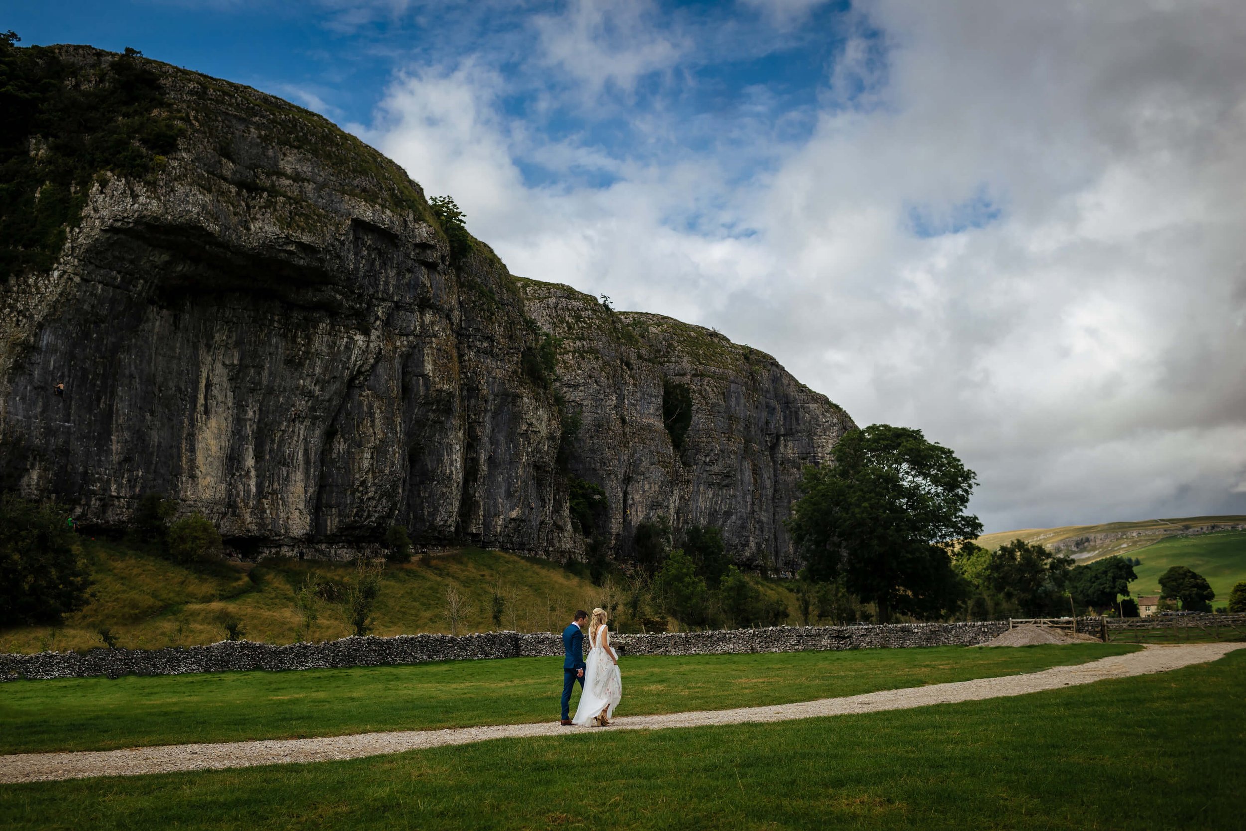 Bride and groom walking in front of Kilnsey Crag on their wedding day