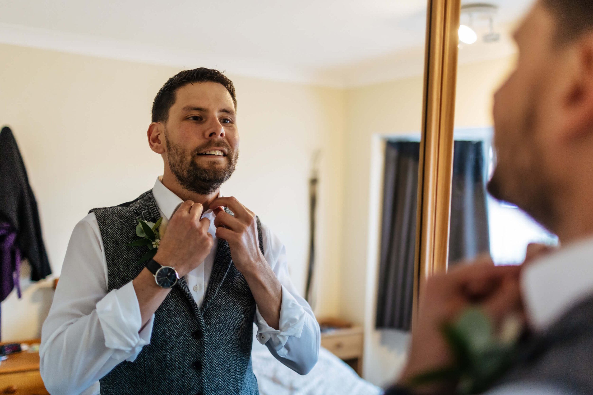 Groom getting ready looking in the mirror and adjusting his collar