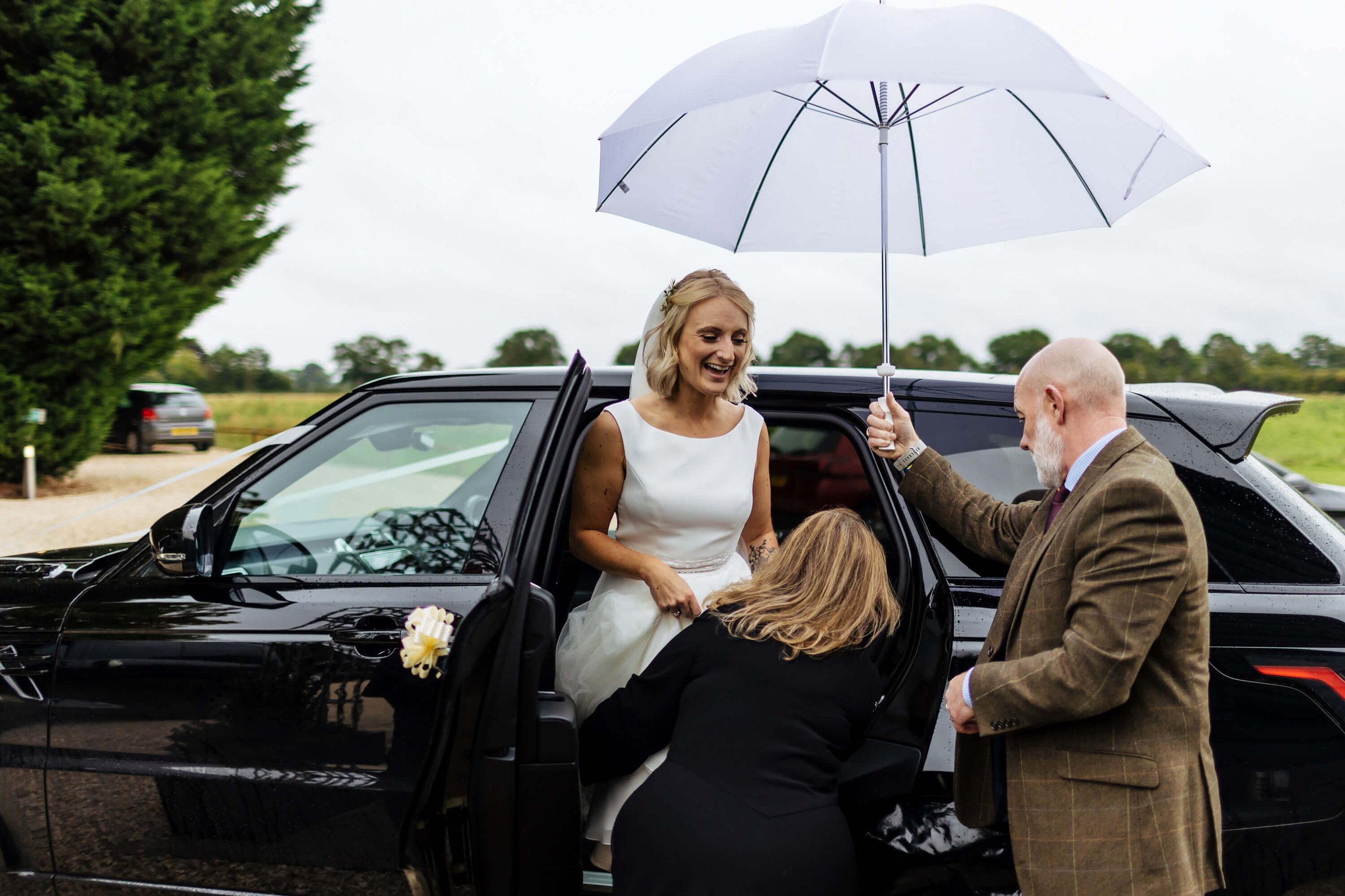 Bride getting out the wedding car under an umbrella