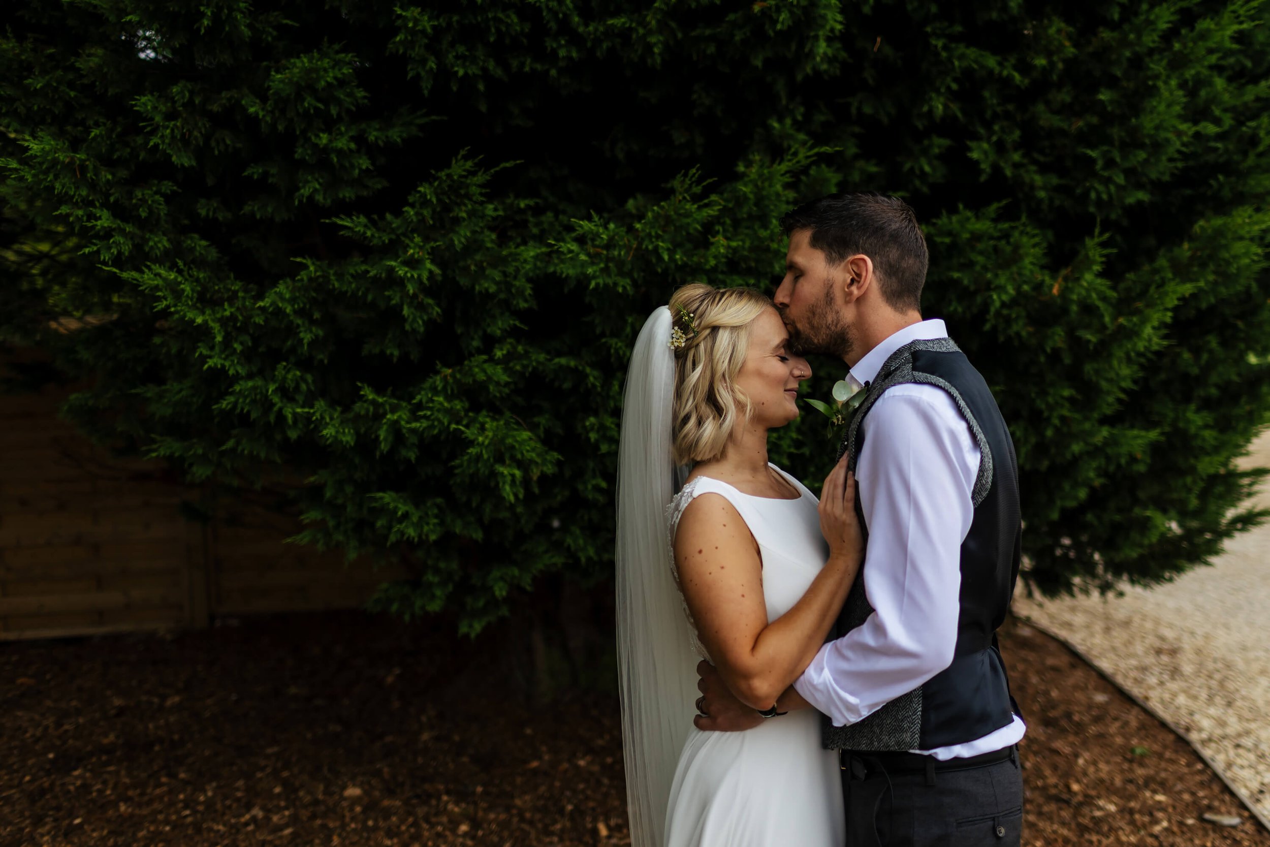 Groom kisses his wife's forehead for a picture
