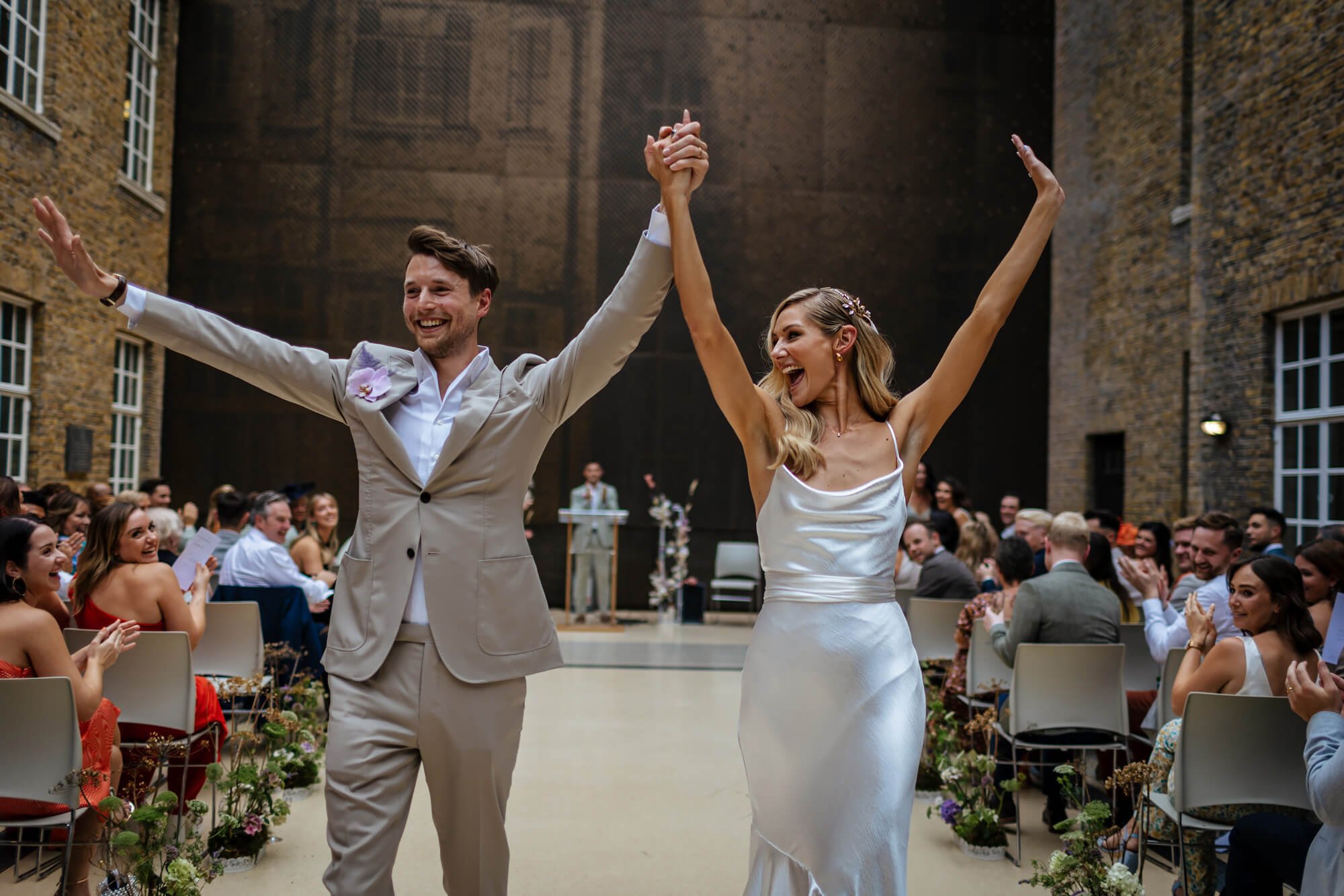 The bride and groom wave their hands in the air as they walk down the aisle