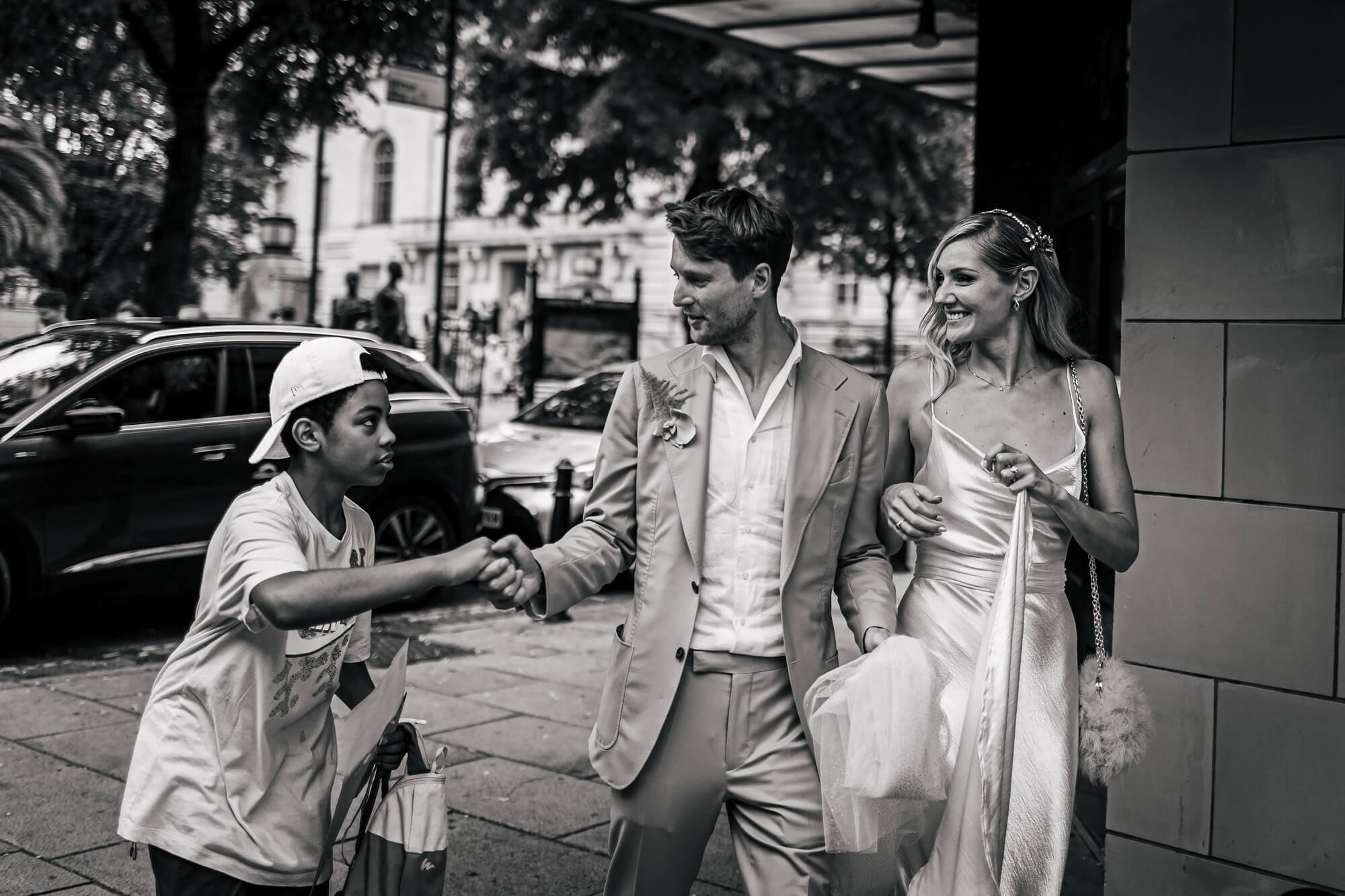 A young boy shakes the grooms hand as they walk through the streets