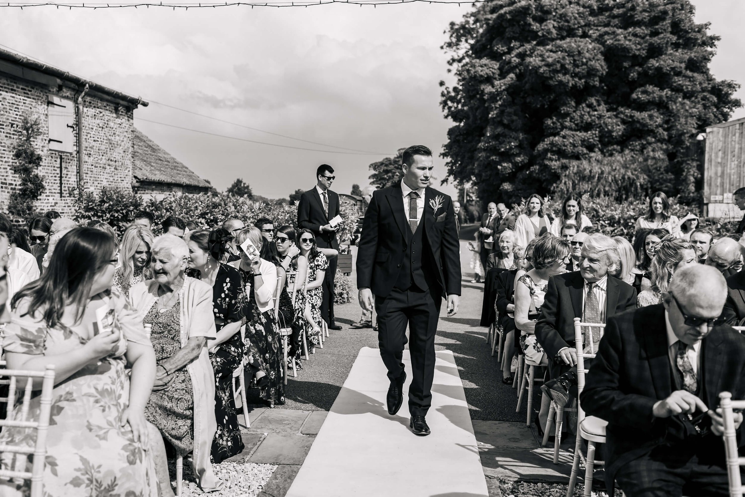 Groom walks down the aisle at his wedding in the sunshine