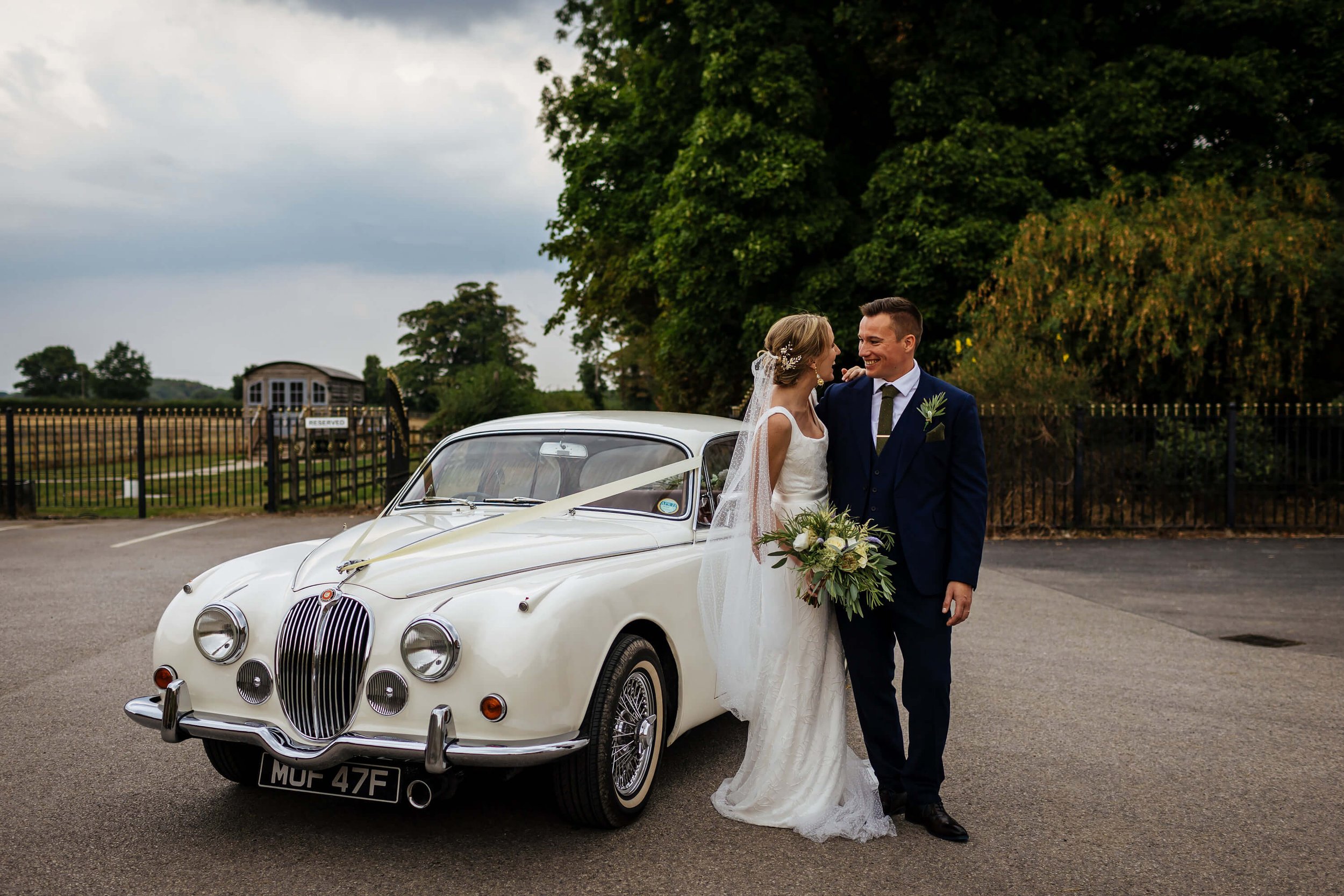 Bride and groom pose for a photo in front of their wedding car