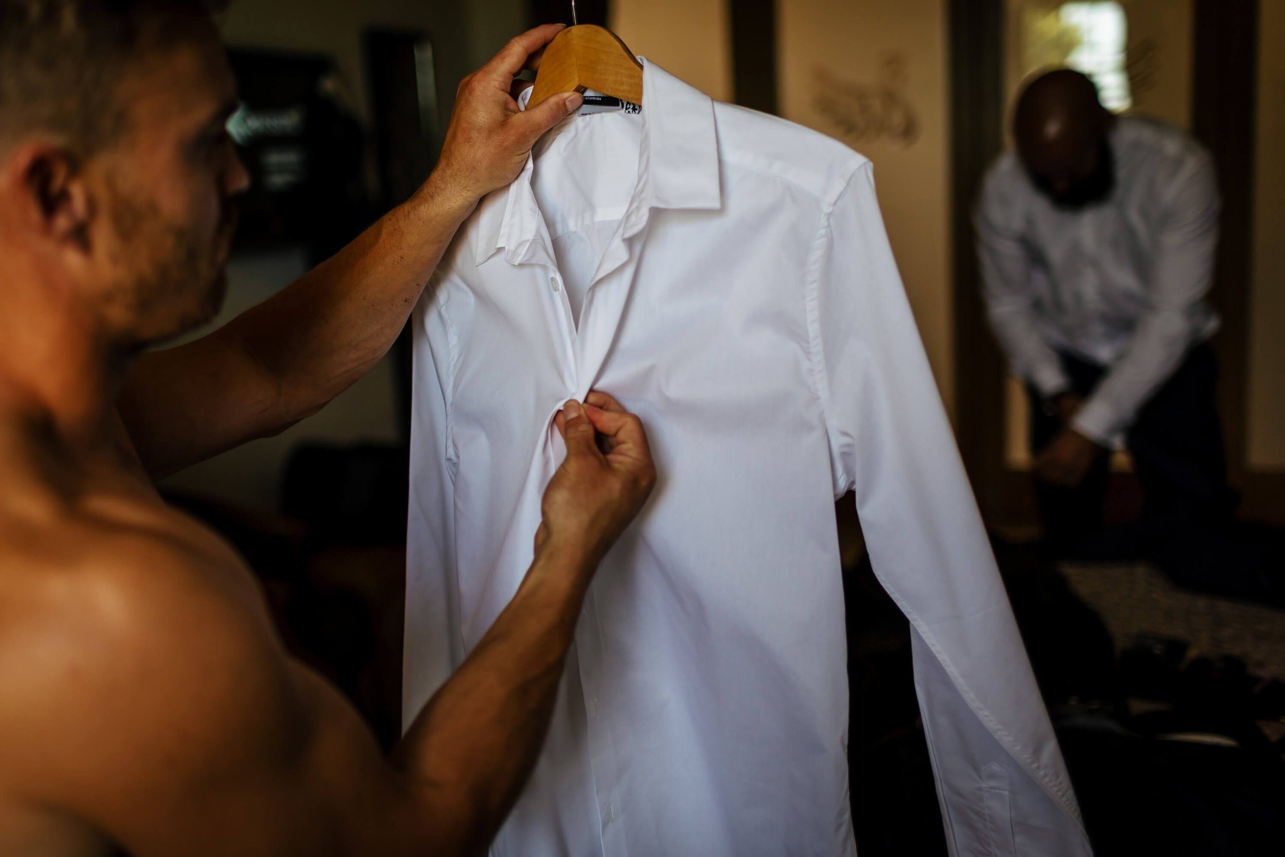 Groom putting his shirt on for a wedding at Swancar Farm