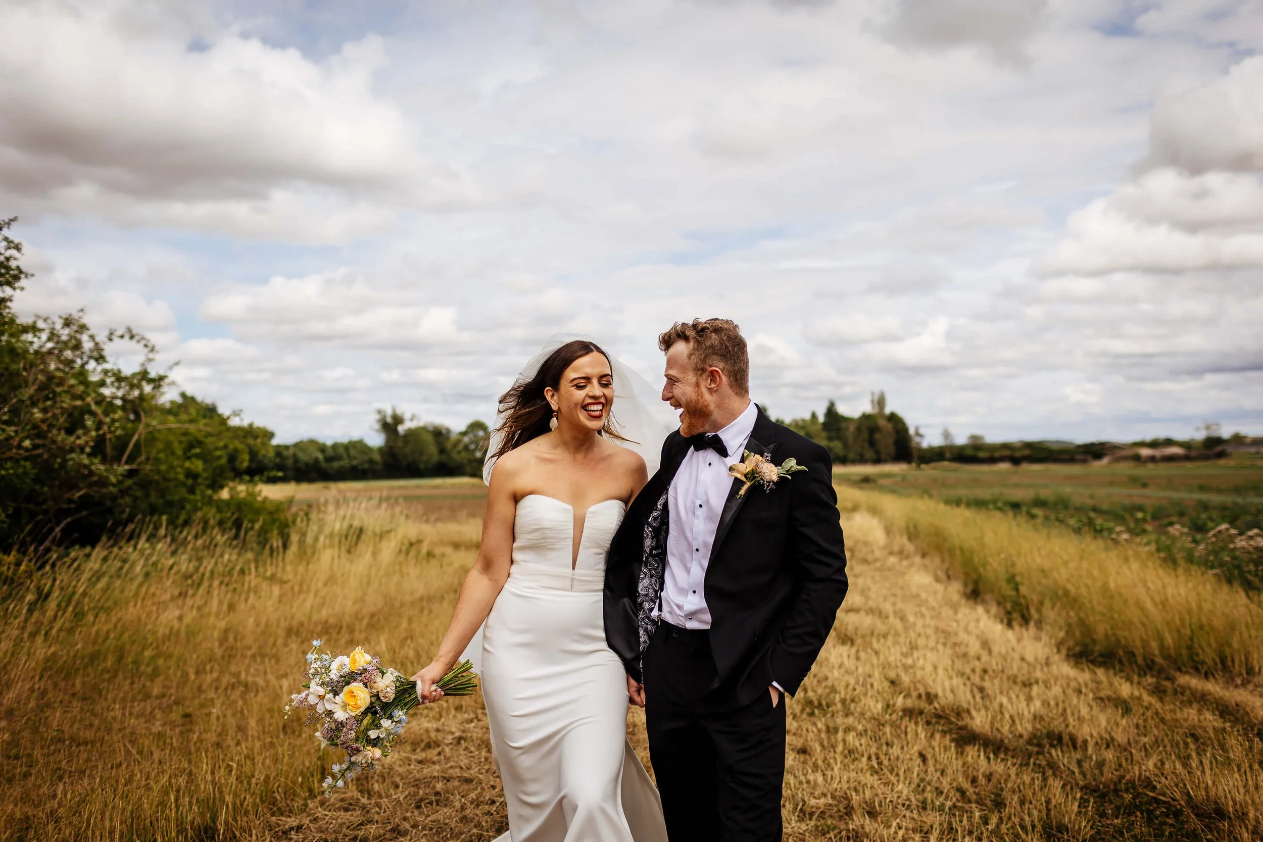 Bride and groom strolling through a field in the sunshine