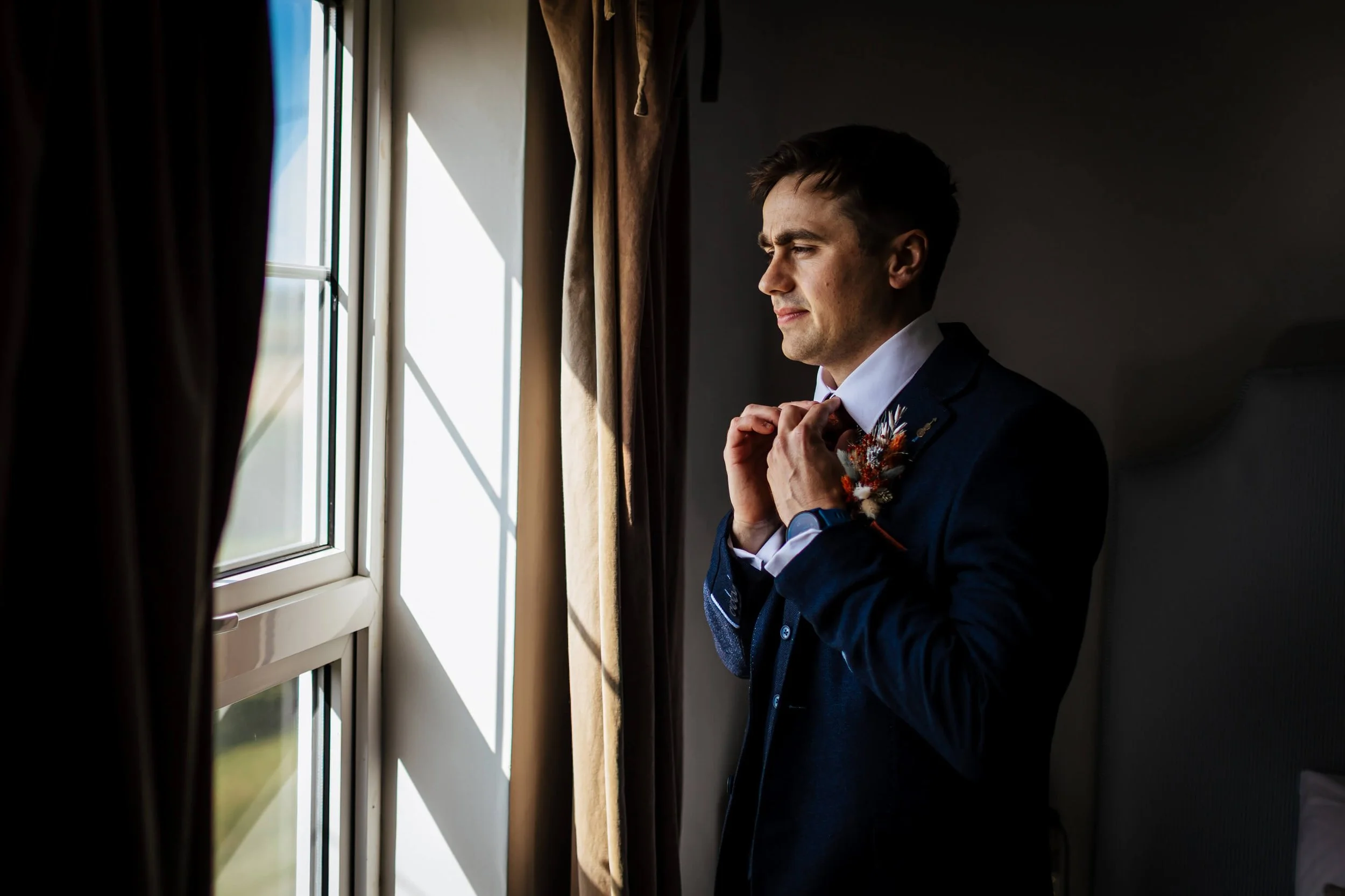 Groom fastening his tie as he gets dressed for the wedding