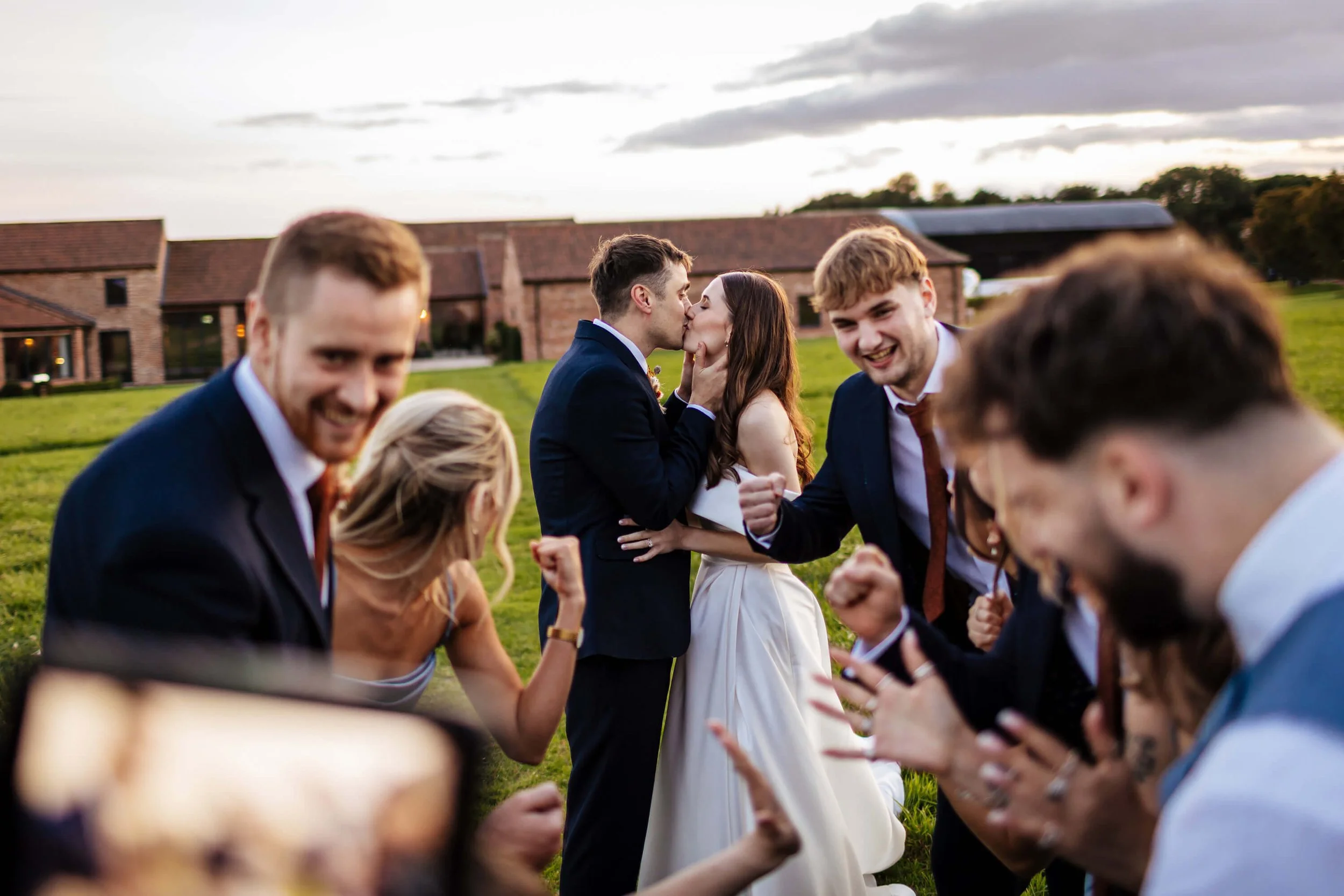 Bride and groom kiss while their friends cheer at their wedding