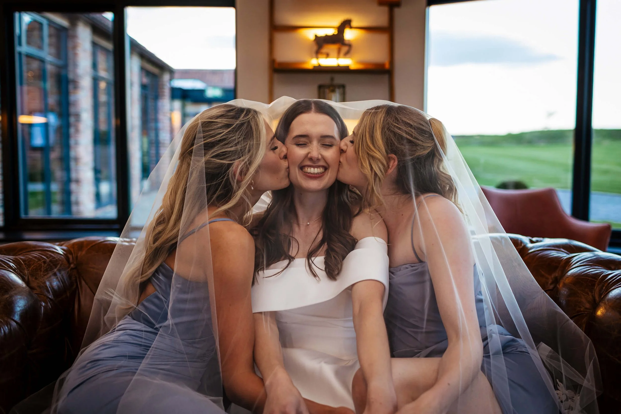 Bridesmaids kissing the bride on her cheek underneath her veil