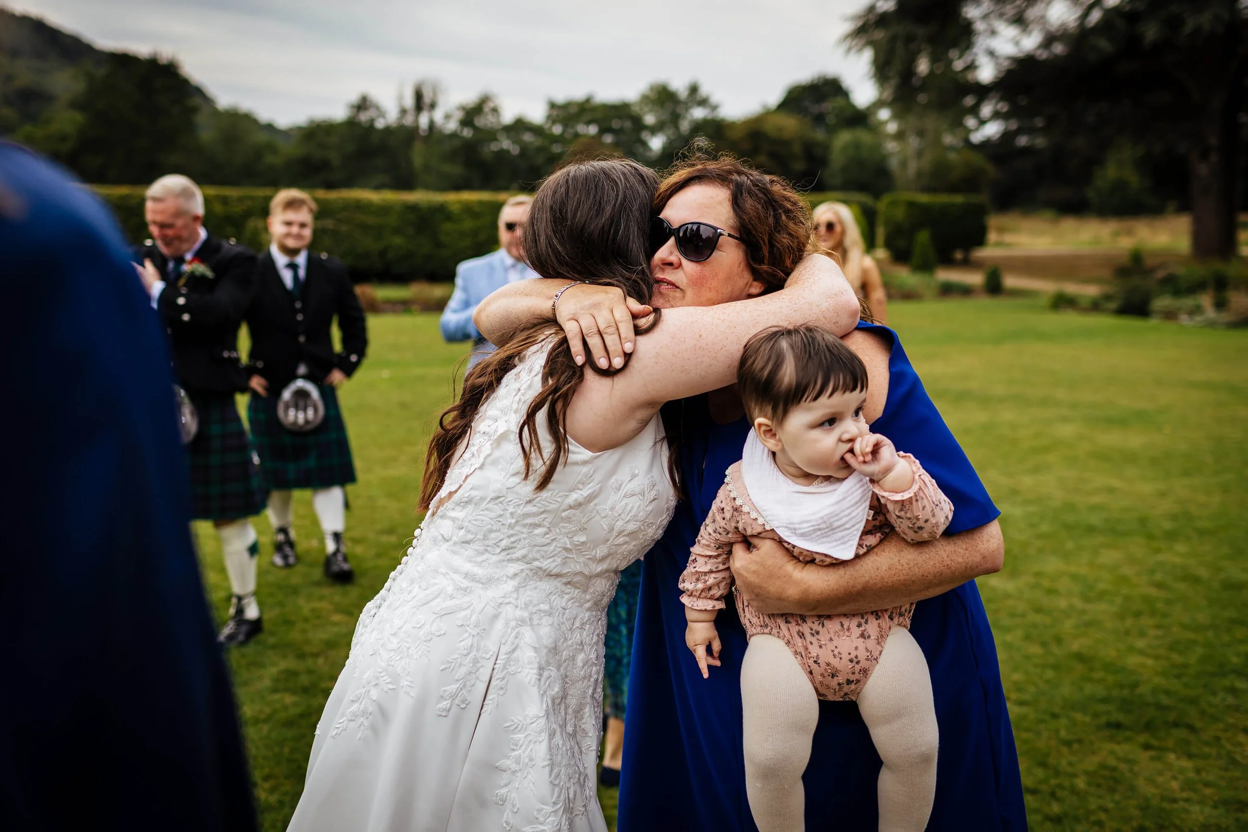 Wedding guests hugging in the gardens at the reception