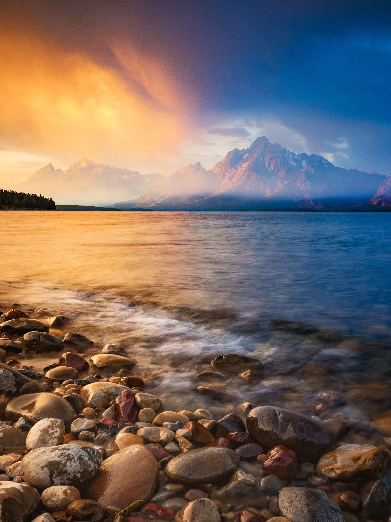 Dramatic sunrise sky over Mount Moran and the Teton Range with a rocky shoreline along Jackson Lake at Colter Bay, Grand Teton National Park, Wyoming, by Ryan L. Smith