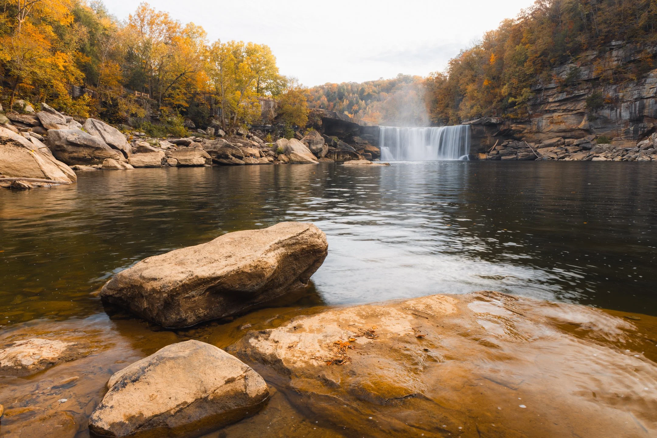 Boulders in the foreground with Cumberland Falls in the distance from the lower beach area, Kentucky, by Ryan L. Smith