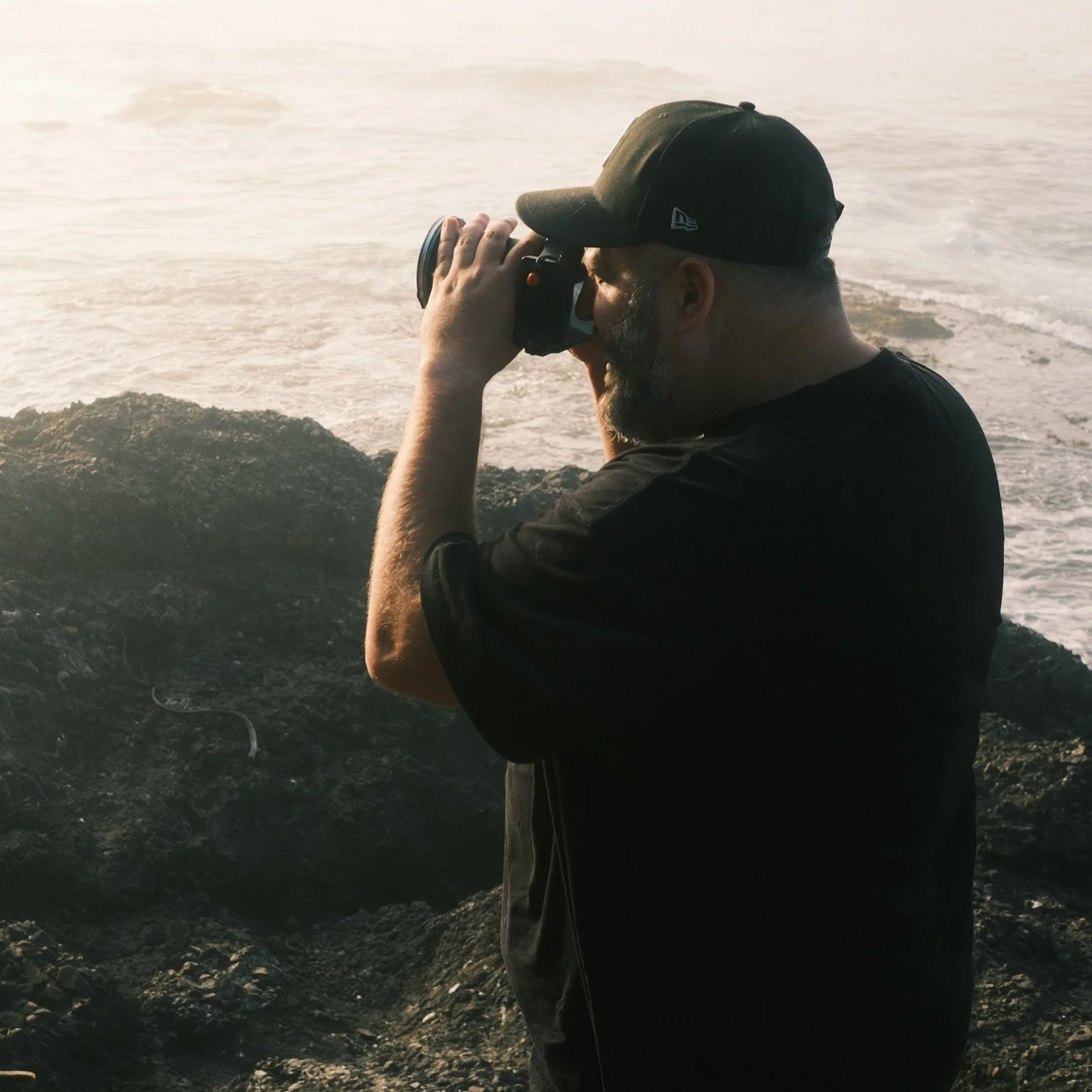 Ryan L. Smith photographing at sunrise on the Oregon Coast cliffs with waves in the background.