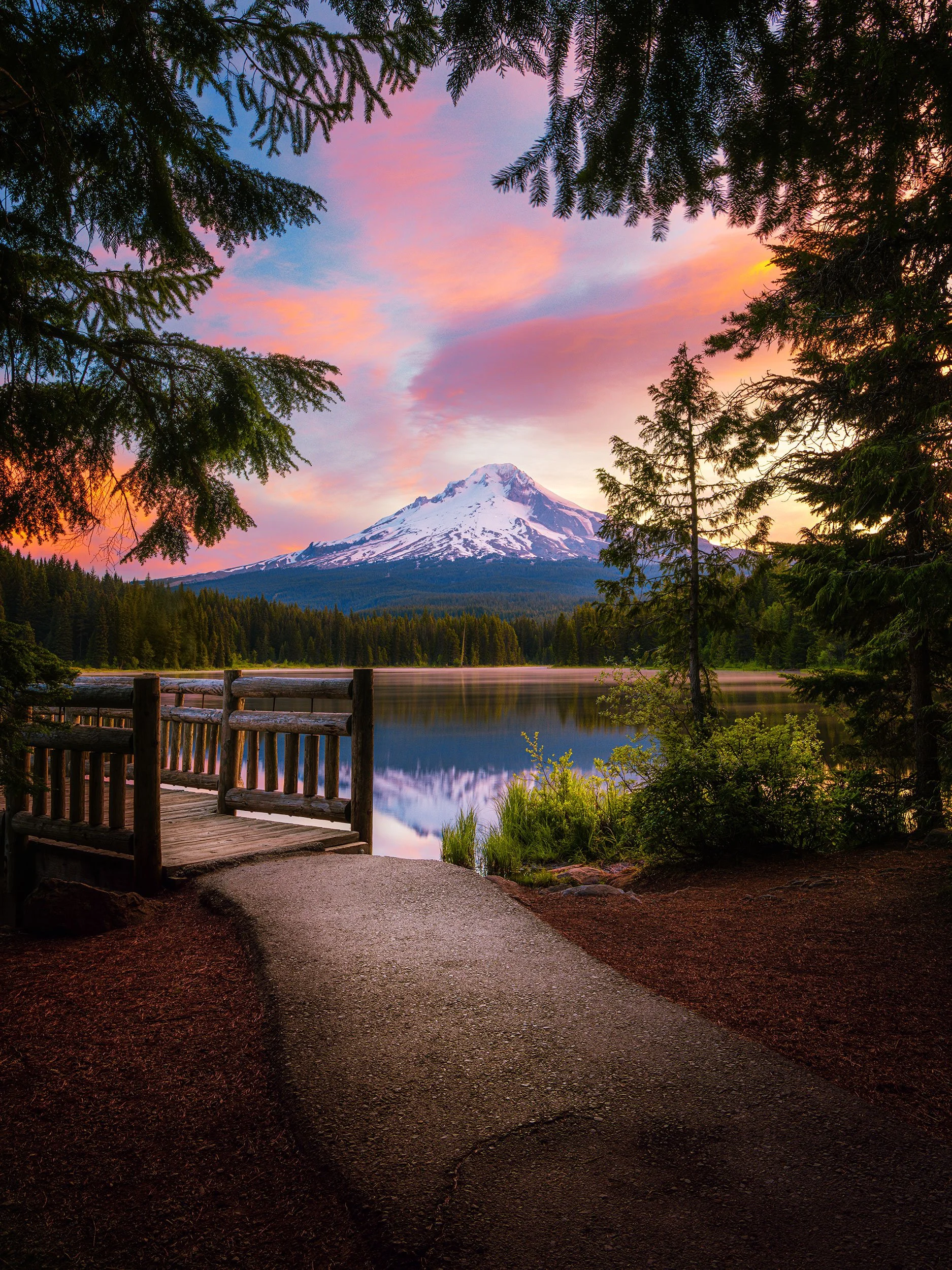 Pink sunrise clouds over snow-capped Mount Hood reflected in Trillium Lake, with a wooden dock and forest path in the foreground, Oregon landscape photography by Ryan L. Smith