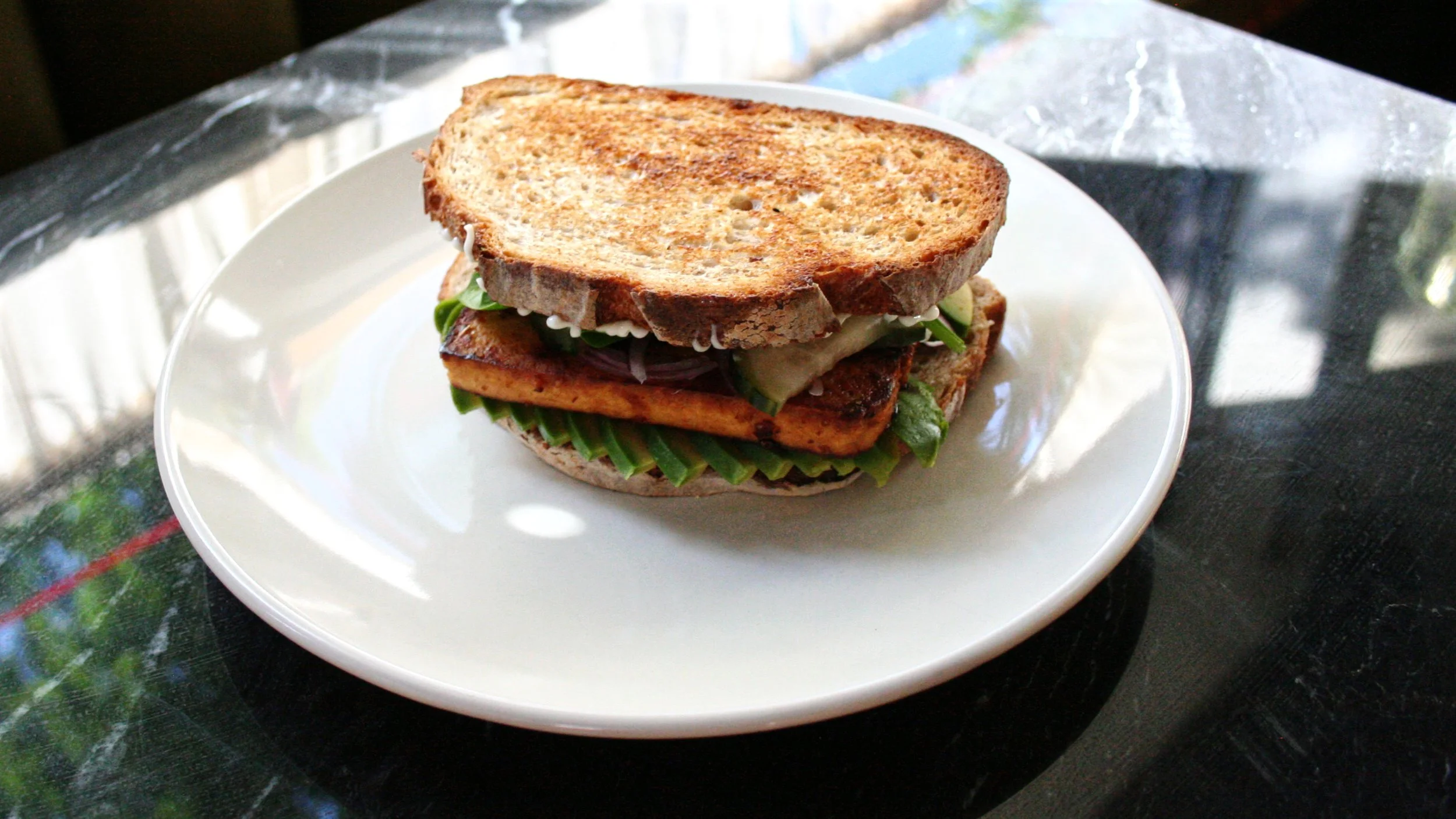 A grilled sandwich with lettuce, tomato, and other vegetables on a white plate.
