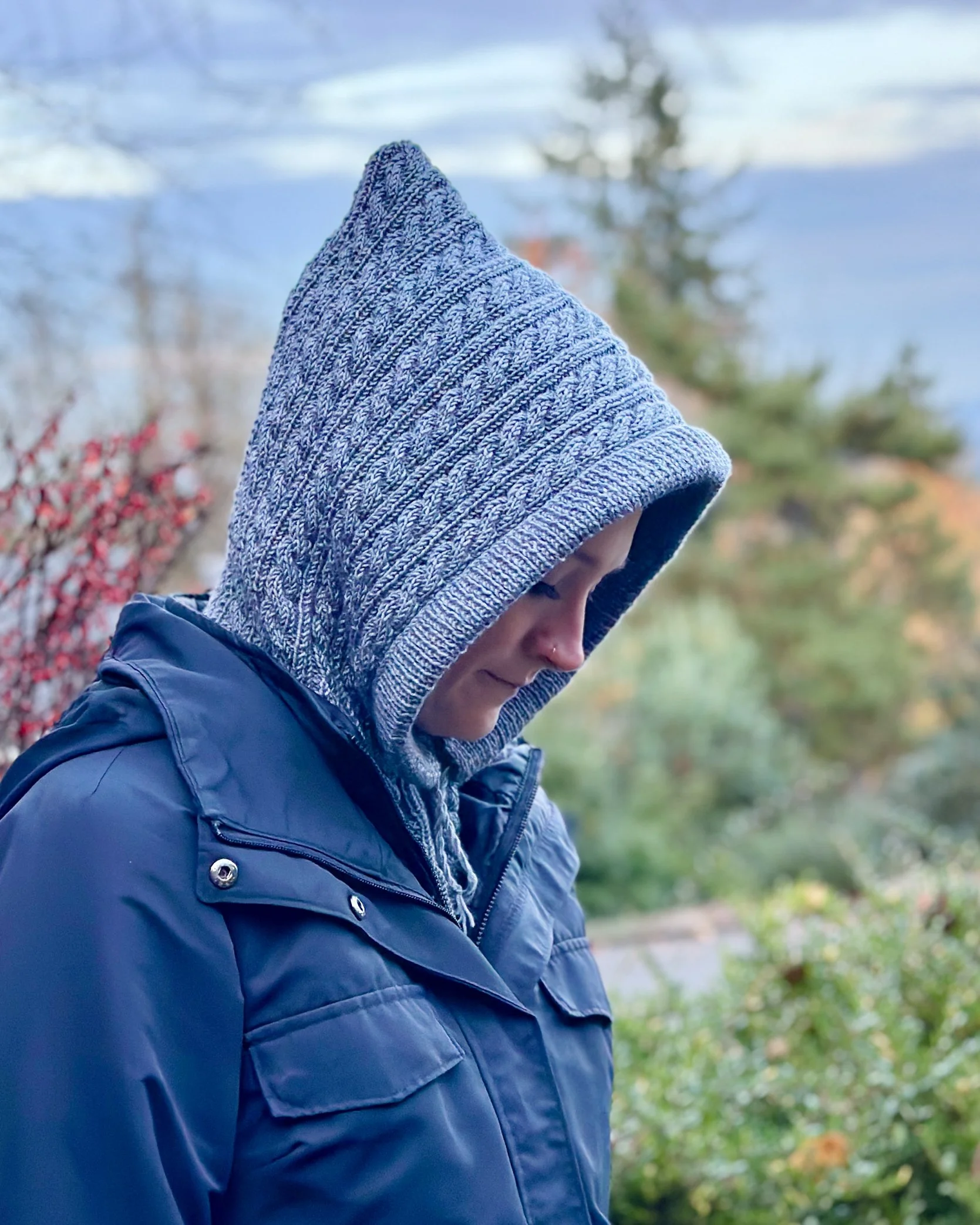 Model wearing blue-grey Tryon Creek Hoodie, an easy hoodie/cowl (balaclava) knitting pattern, that can be worn as a cowl with the hood up or down.