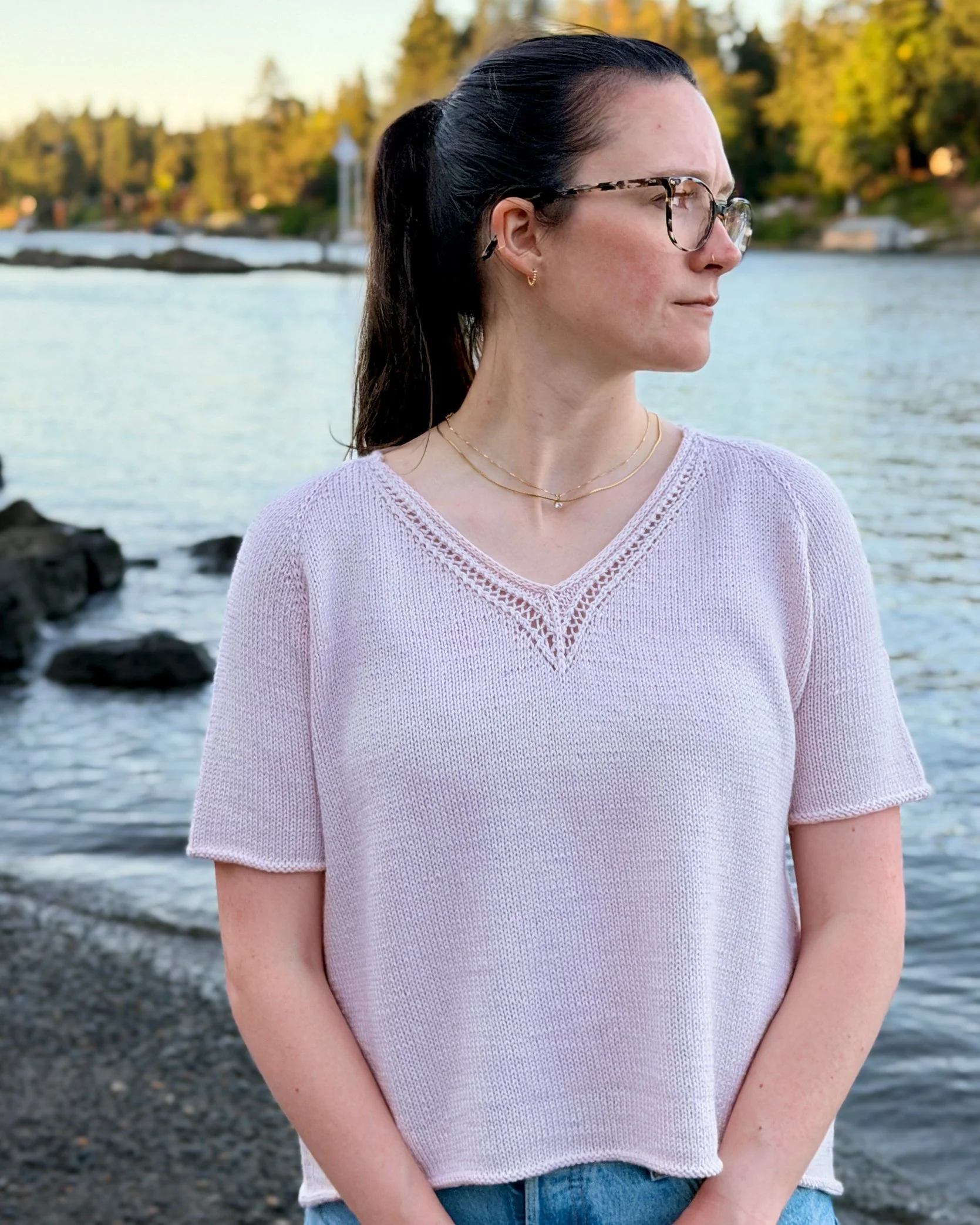 Classic Lace Tee, a V-Neck Knit Top / Pullover / Sweater Pattern in a blush colored yarn by Rosy Green Wool on model in front of river