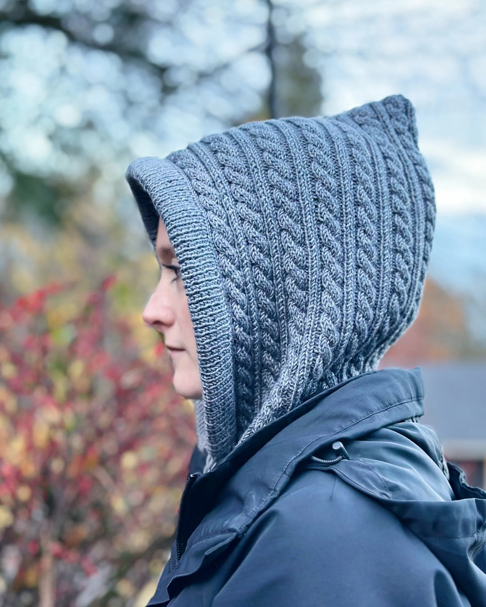 Tryon Creek, an easy cabled hoodie/cowl (balaclava) knitting pattern, that can be worn as a cowl. Model wearing blue-grey version with hood up.