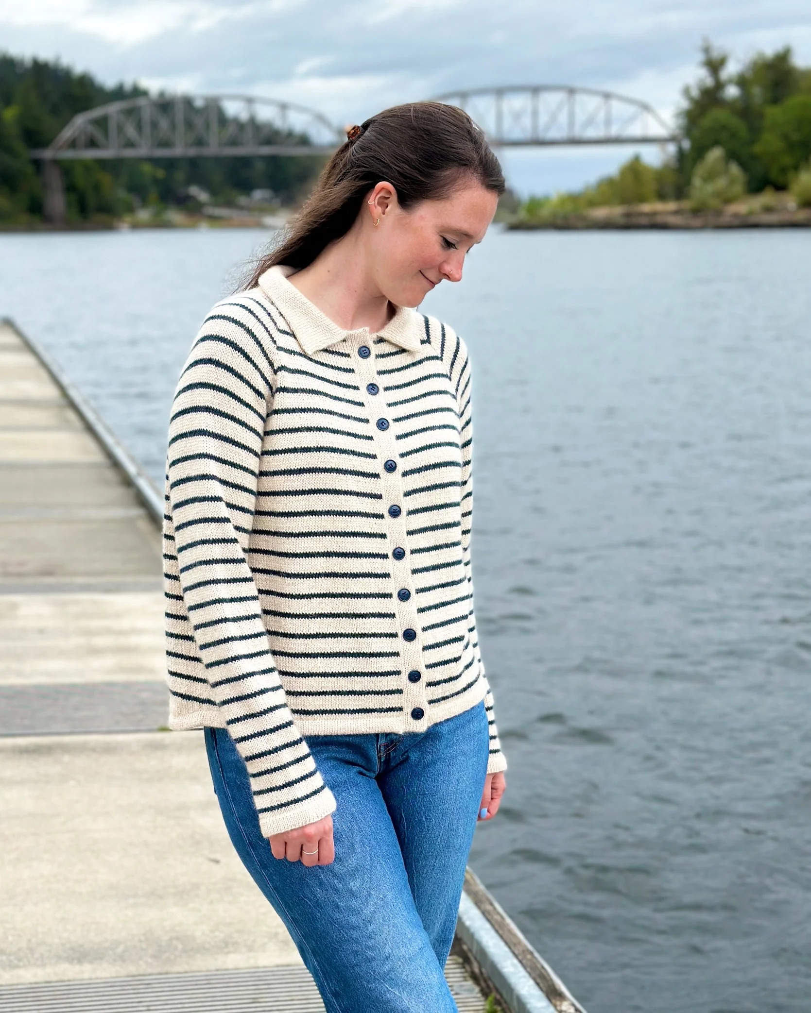 Model smiling by the river in King Tides cardigan knitting pattern with front buttoned and worn as a striped pullover.