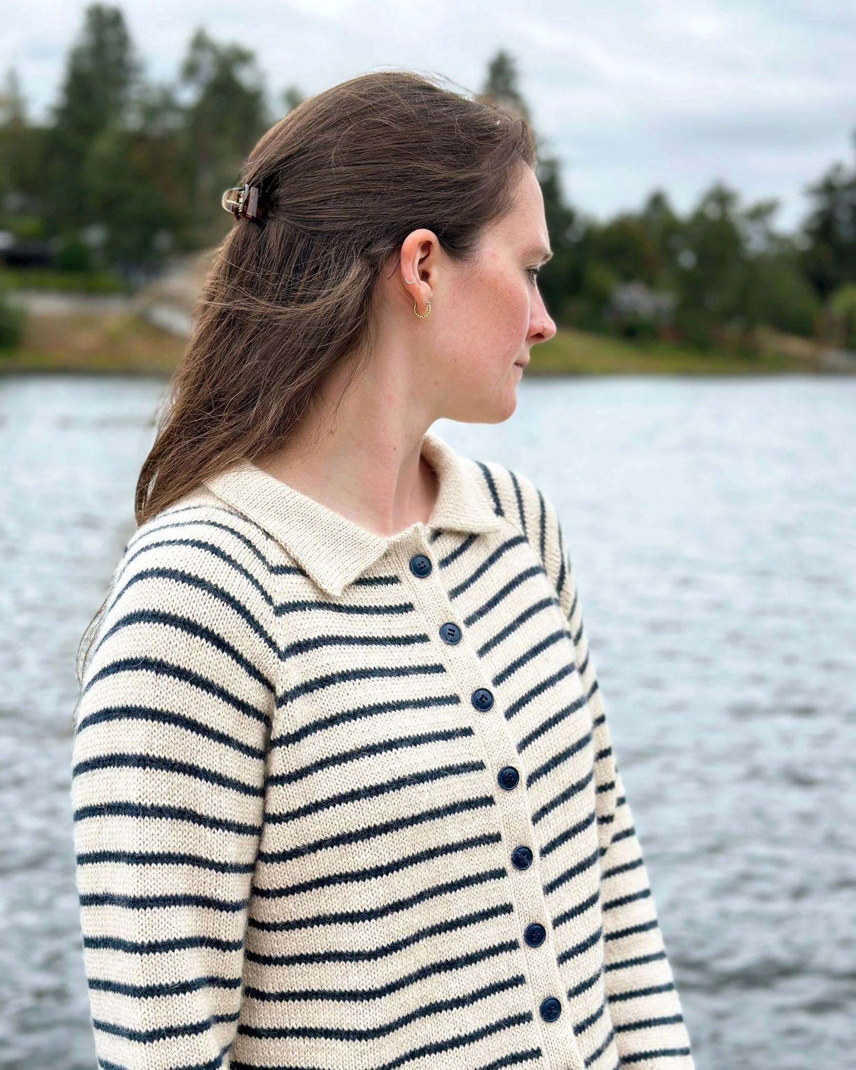 Model watching the river while wearing King Tides cardigan knitting pattern stripes and buttoned front.