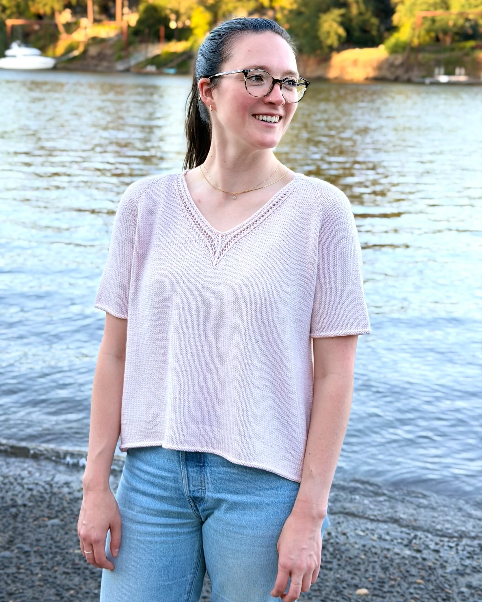 Classic Lace Tee, a V-Neck Knit Top / Pullover / Sweater Pattern in a blush colored yarn by Rosy Green Wool on model in front of river