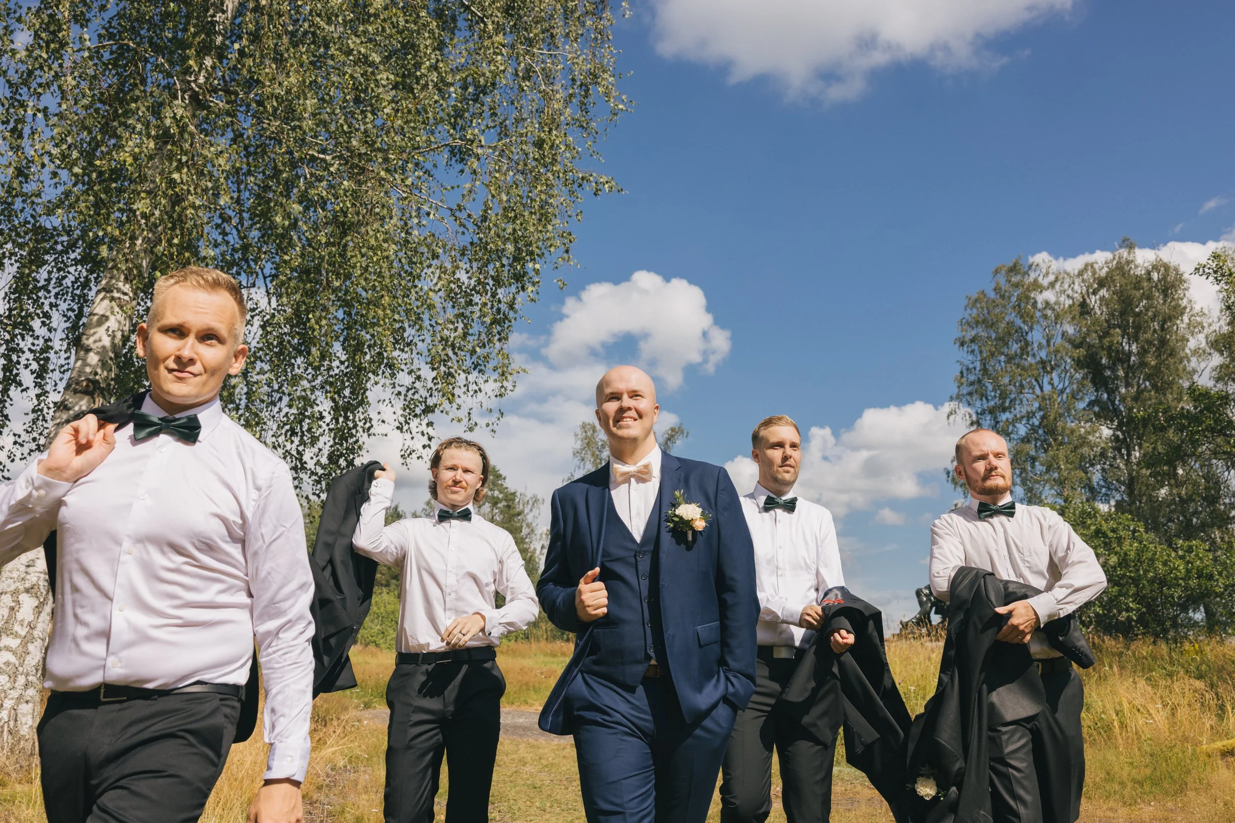 Hurmajaisten hääryhmän kuva ulkona vihreässä maisemassa ja sinisellä taivaalla.