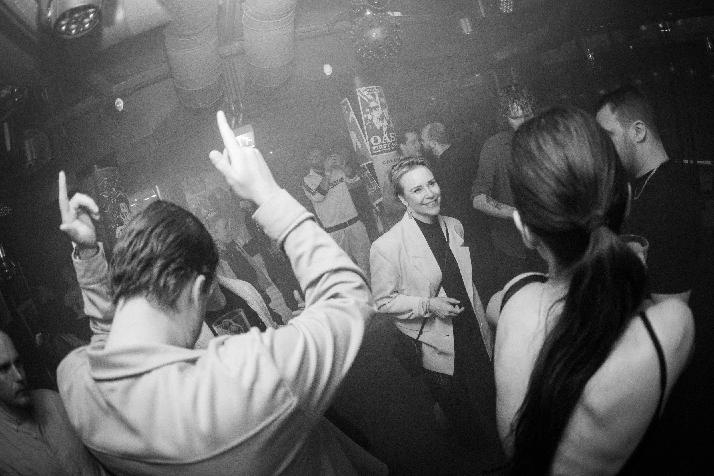 Gruppia ihmisiä tanssimassa ja juttelemassa klubilla, mustavalkoinen kuva