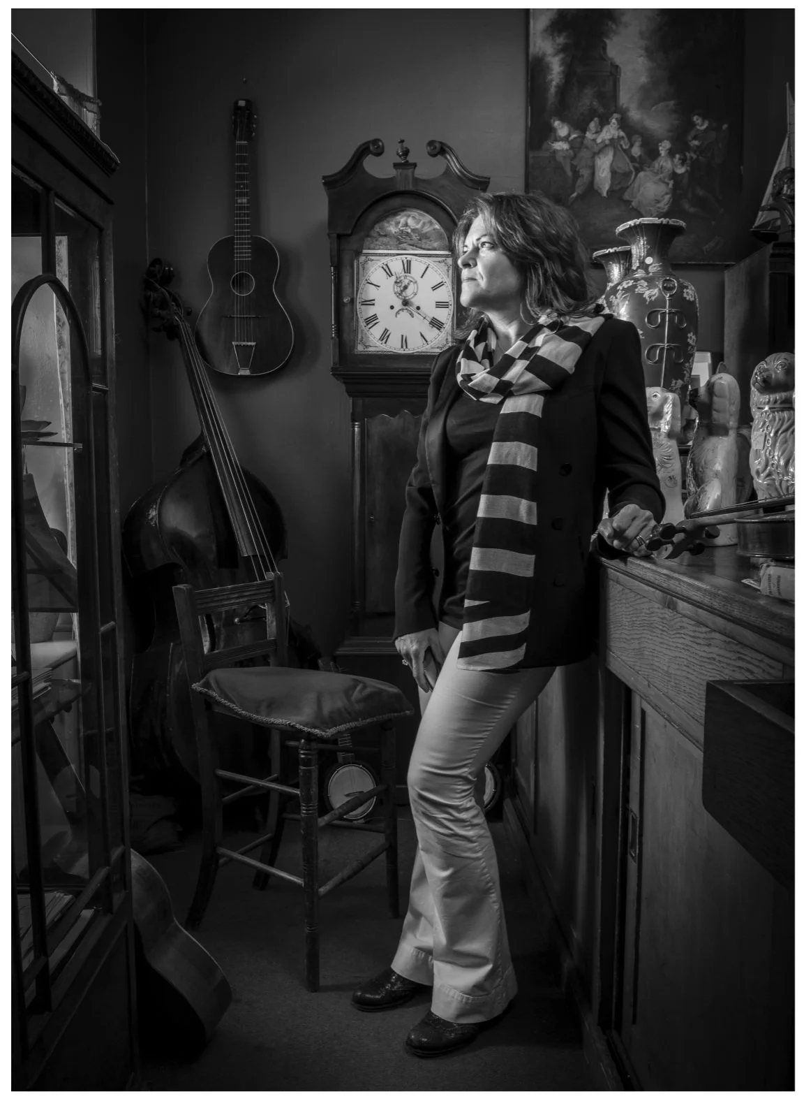 Woman wearing a long stripey scarf in an antique shop stands looking out window