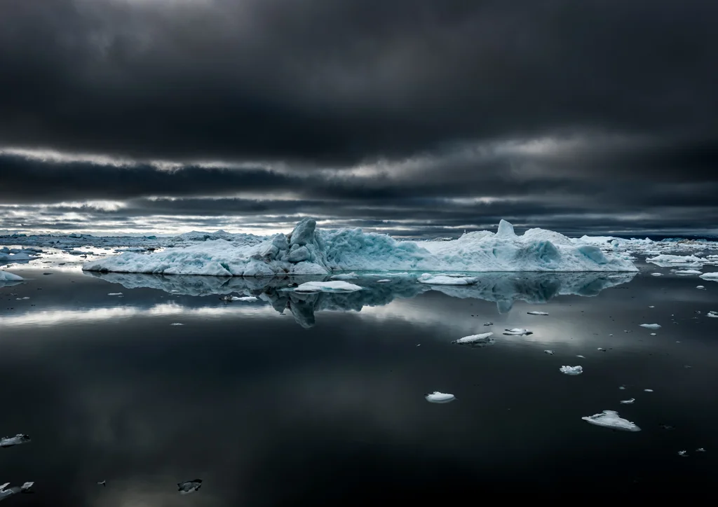Turquoise blue uicebergs floating in dark black sea with dark skies above