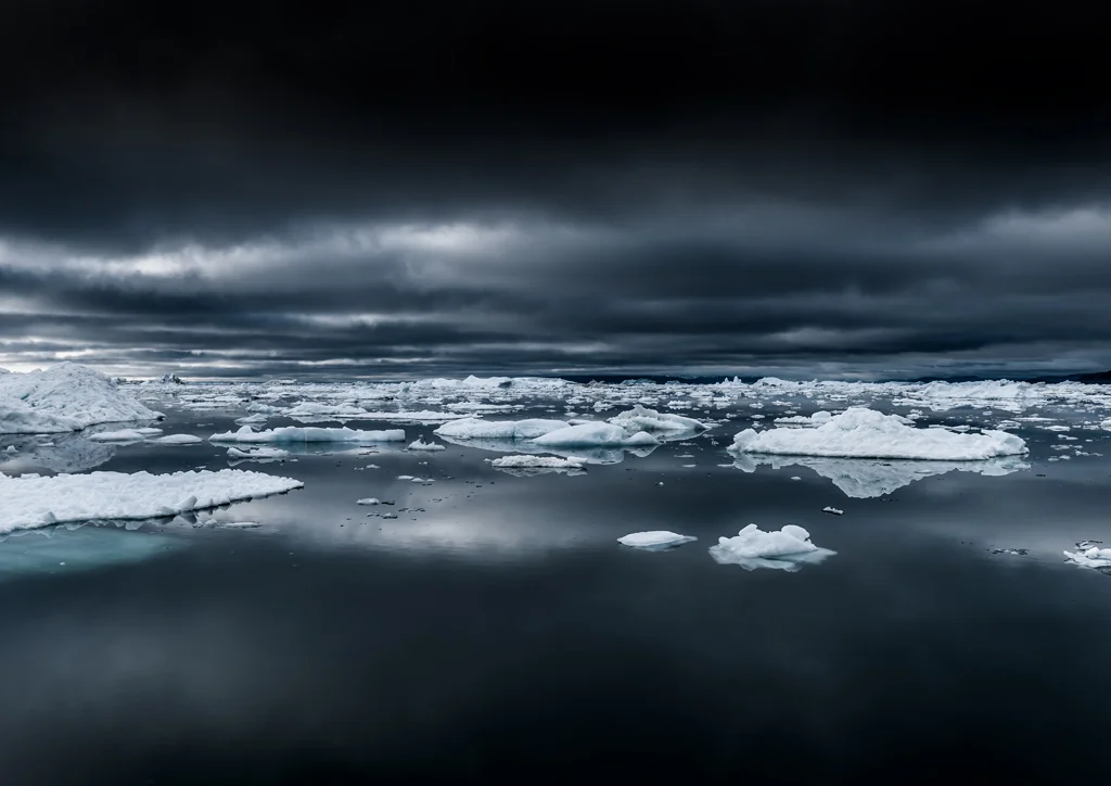ice flow with icebergs floating in dark sea with dark clouds looming overhead
