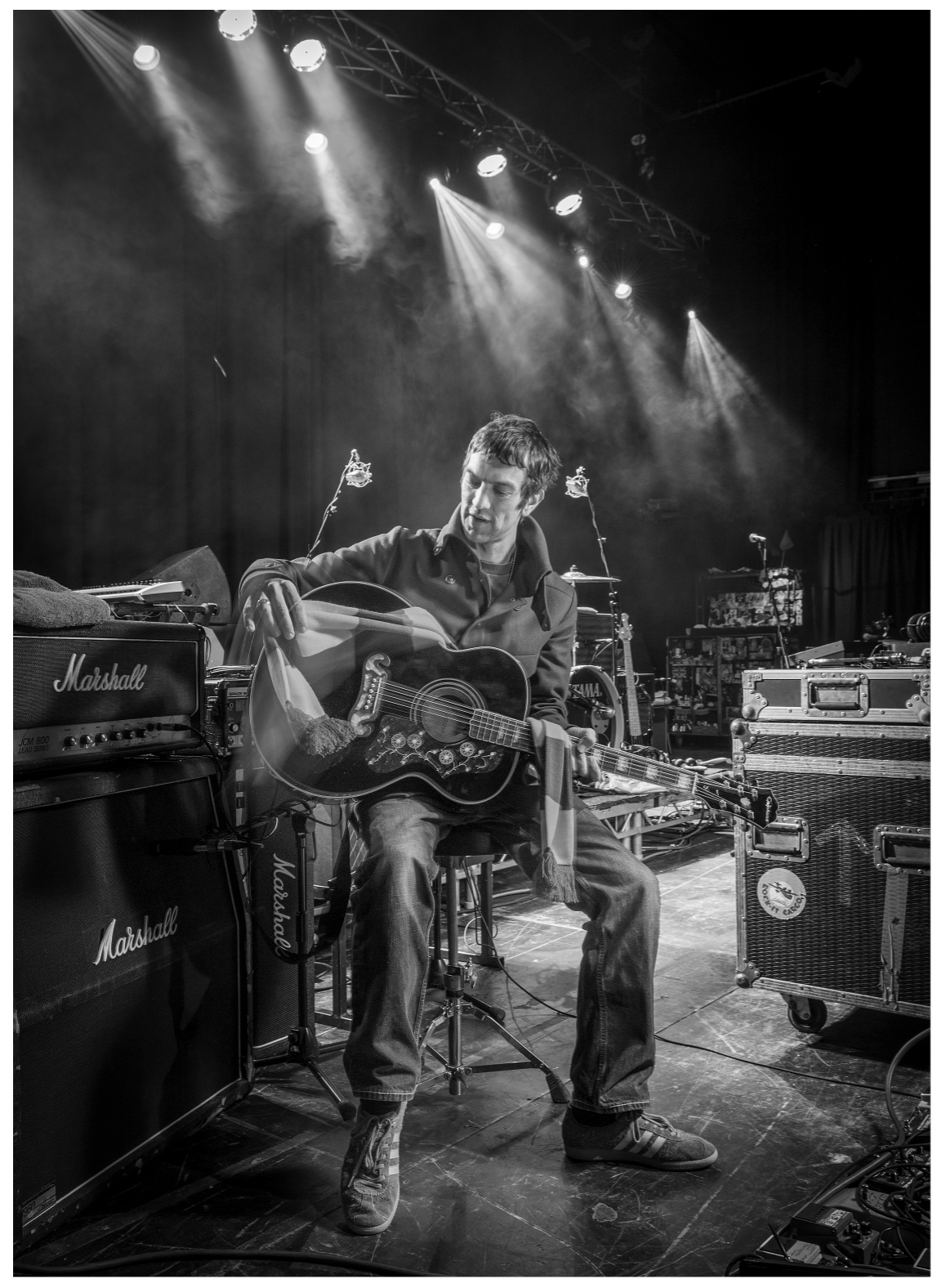 Rock singer sits on stage draping football scarf over his guitar