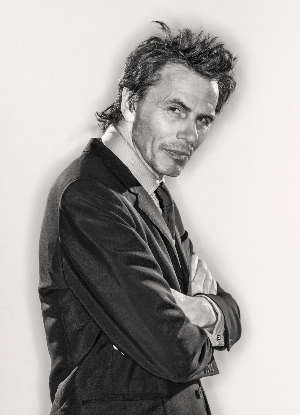 John Taylor of rock band Duran Duran wearing a suit with arms folded looks at camera