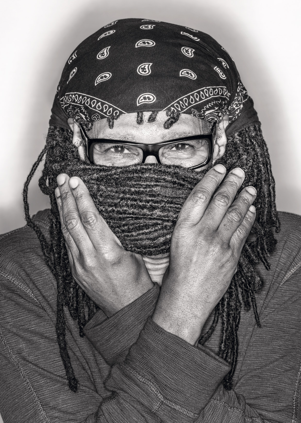 Guitarist Nile Rogers holding his dreadlocks across his mouth. He is wearing glasses and a bandana