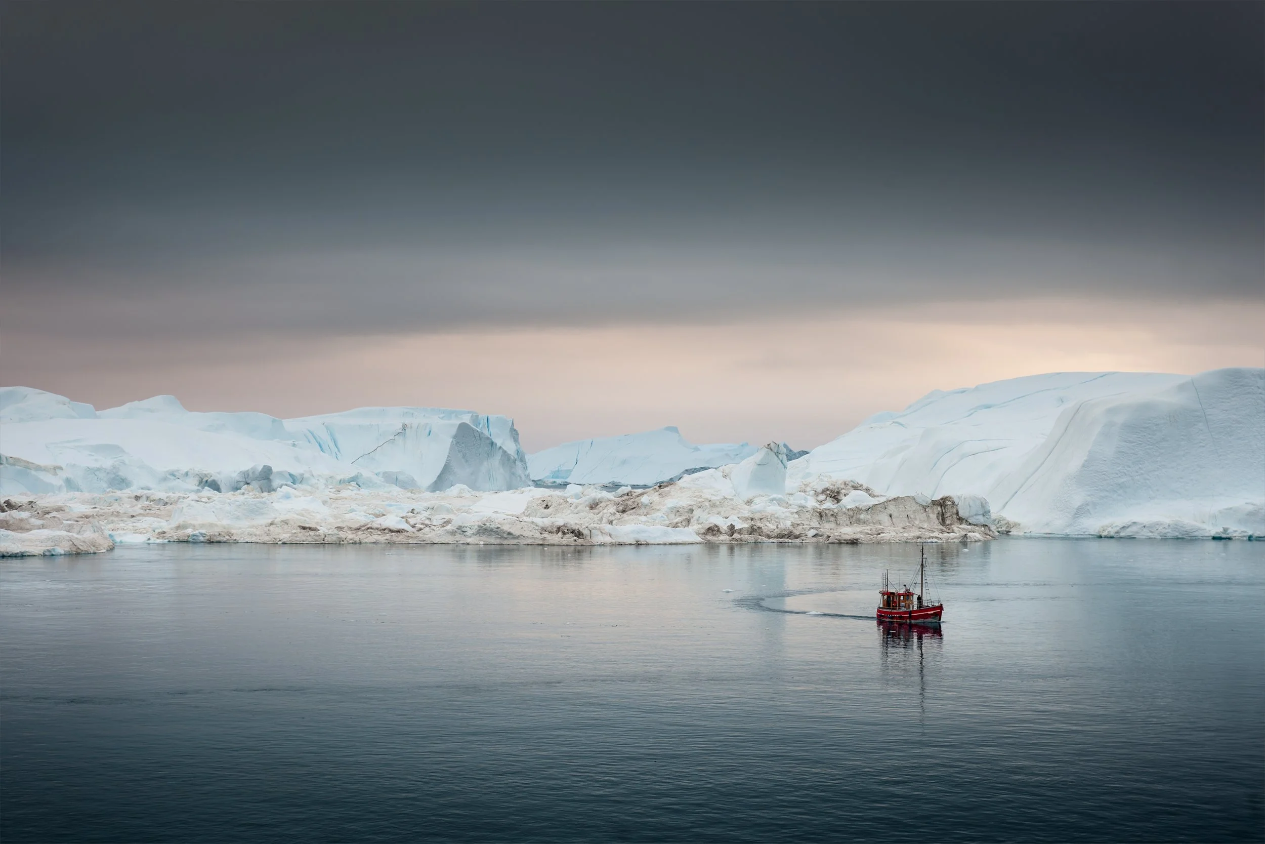 Boat at sea sailing amongst huge icebergs